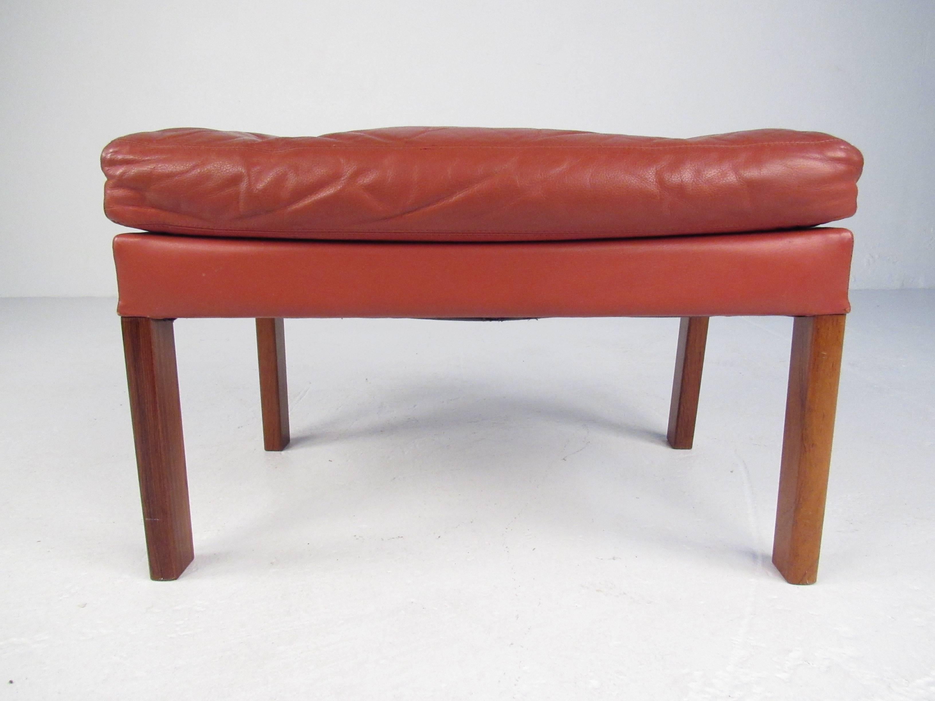 This Mid-Century Modern ottoman features hardwood legs and supple tufted leather upholstery. Comfortable and stylish addition to any seating arrangement perfect for use as a footstool or occasional seat. Please confirm item location (NY or NJ).