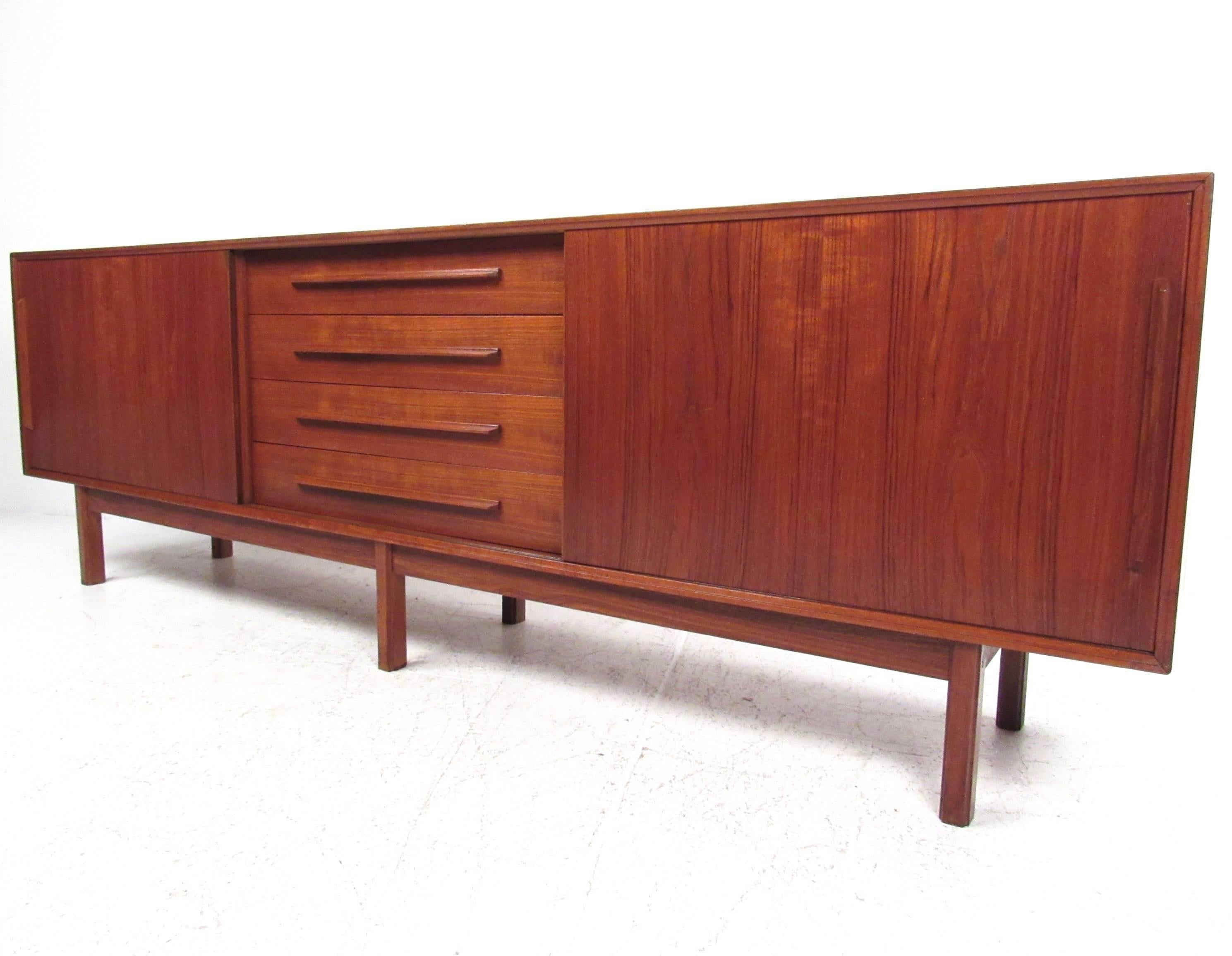 This vintage teak sideboard features a stunning finish with spacious storage cabinets perfect for any setting. Four wide center drawers feature dove tail construction and carved drawer pulls. The spacious shelves offer plenty of room for living room