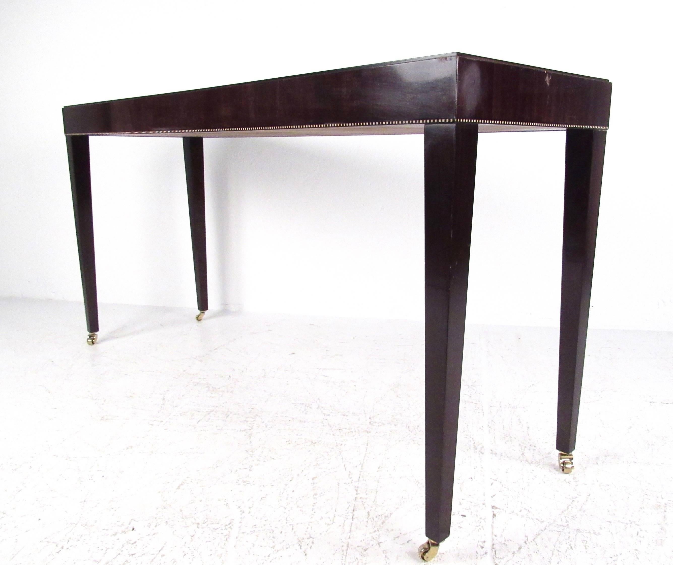 This stunning console table features shapely legs, unique trim, and a dark lacquer finish. Vintage elegance perfect for entry way hall or living room use. Made in the USA by Council furniture this unique table features brass casters for easy