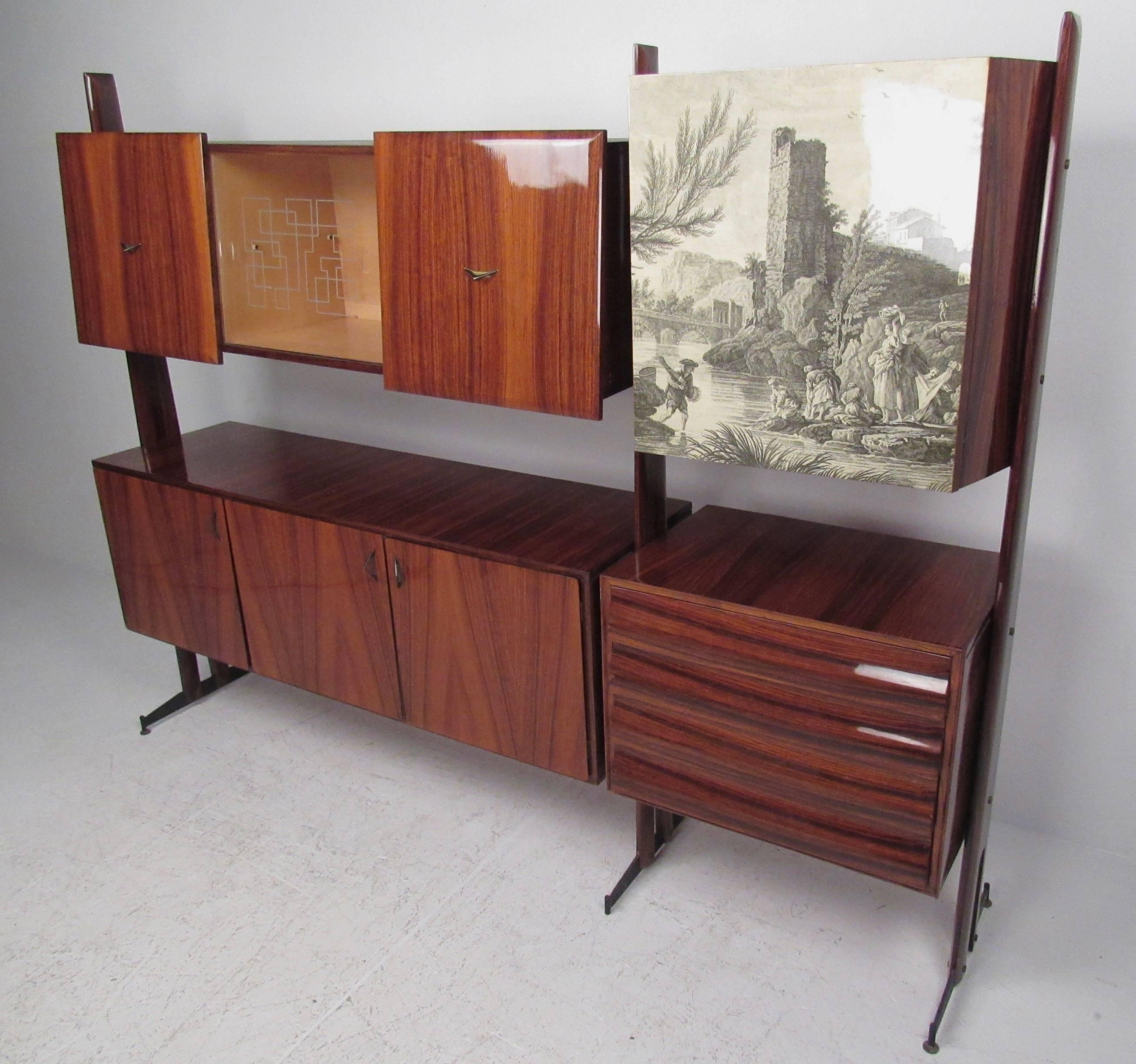 This vintage Italian wall unit features stunning Mid-Century design and offers a modular cabinet display perfect for storage in any modern setting. Rich lacquered wood finish is complimented by illustrated cabinet front bar, while the sliding glass