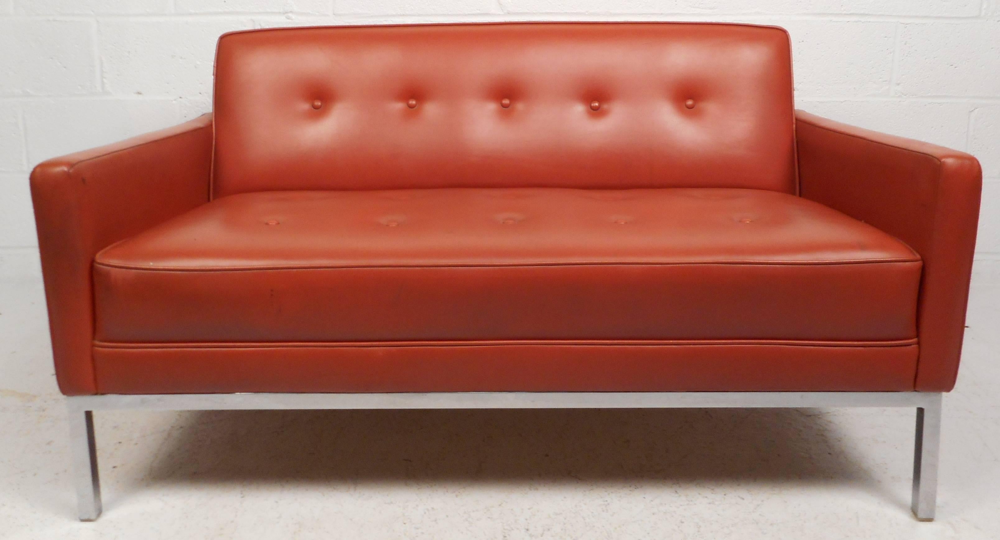 This elegant Mid-Century sofa features tufted vinyl upholstery and chrome legs. The stylish blood orange color and slanted backrest add to the allure of this piece. The versatile size of this love seat offers the ability to be used as a small sofa