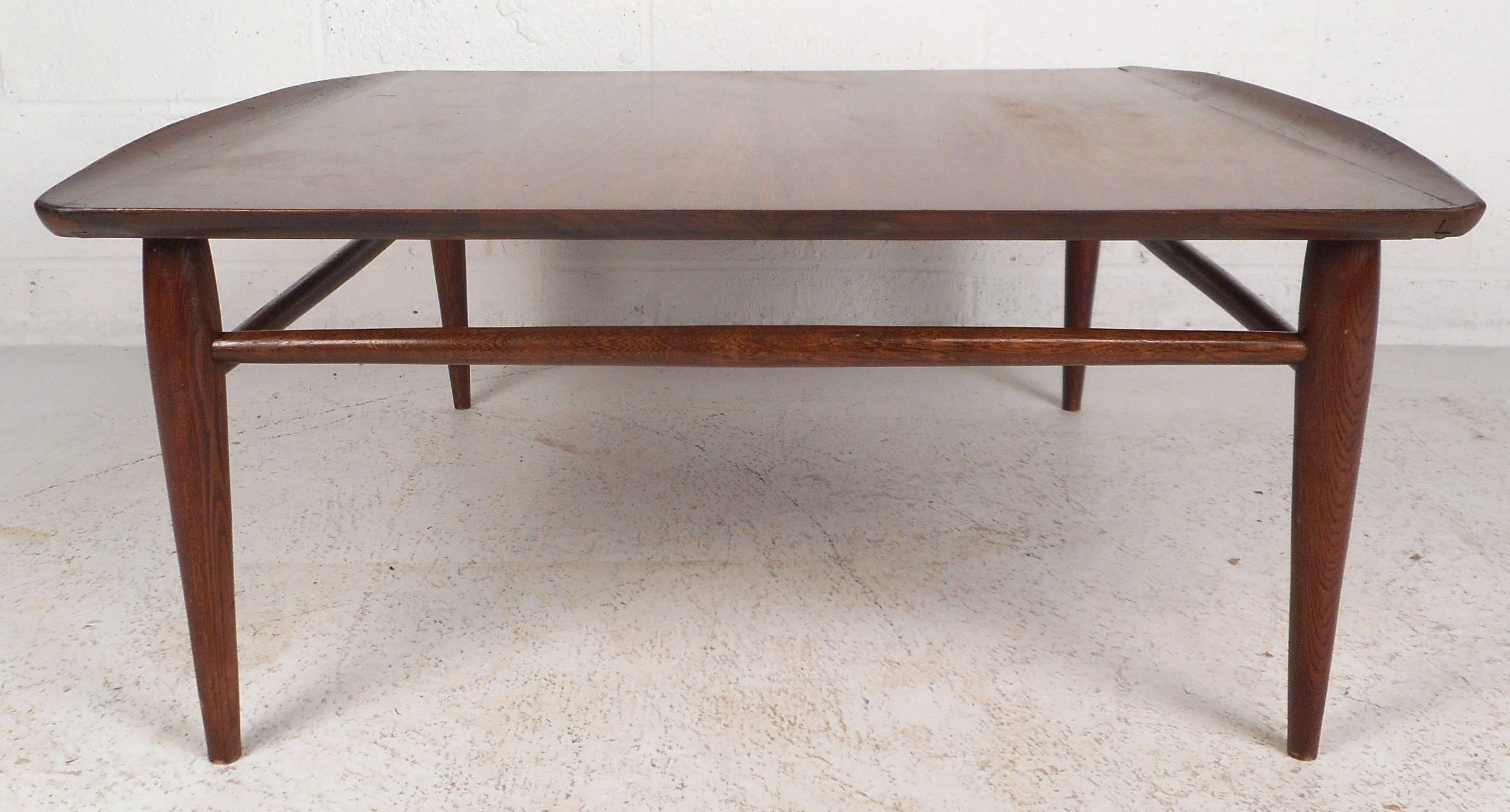 Beautiful vintage modern coffee table features unique raised edges and tapered legs. Sleek design with stretchers between each leg ensuring sturdiness without sacrificing style. The gorgeous walnut wood grain is sure to compliment any modern