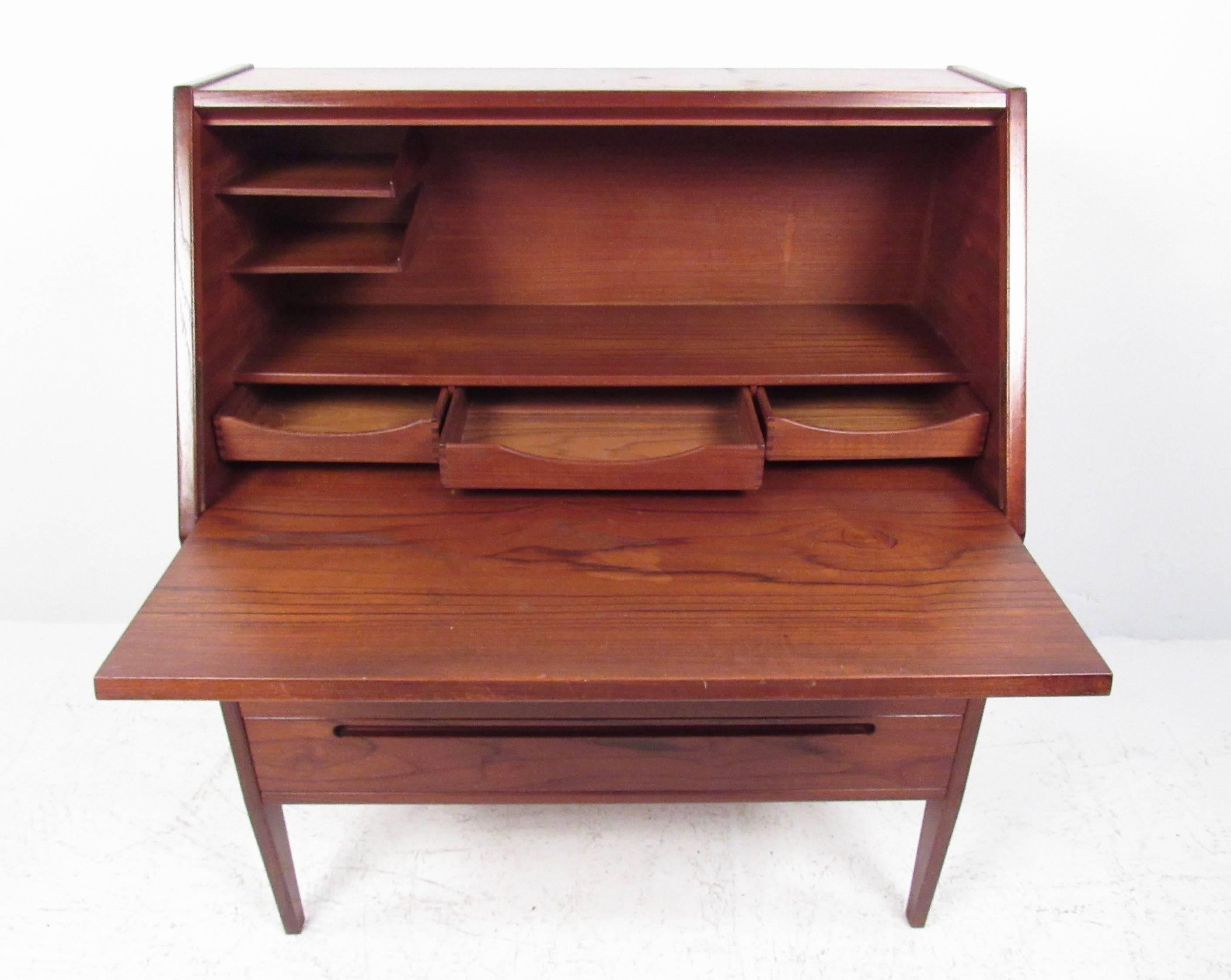 This vintage modern teak desk makes a stylish yet compact addition to any interior. Providing a unique drop front writing area that conceals a well-organized workspace, along with three spacious drawers for storage, this Danish modern secretary desk