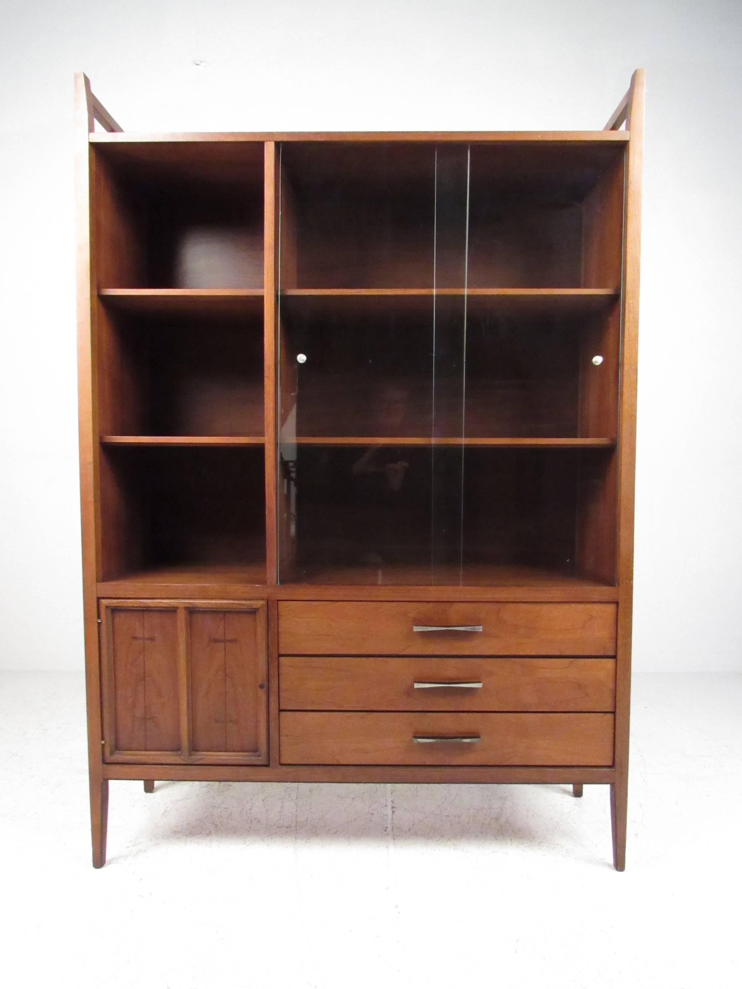 This vintage modern walnut cabinet features spacious storage shelves, lower cabinet and drawers for storage, and a stylish Mid-Century design. Unique drawer pulls and inlaid bowtie details add to it's vintage American charm. Please confirm item