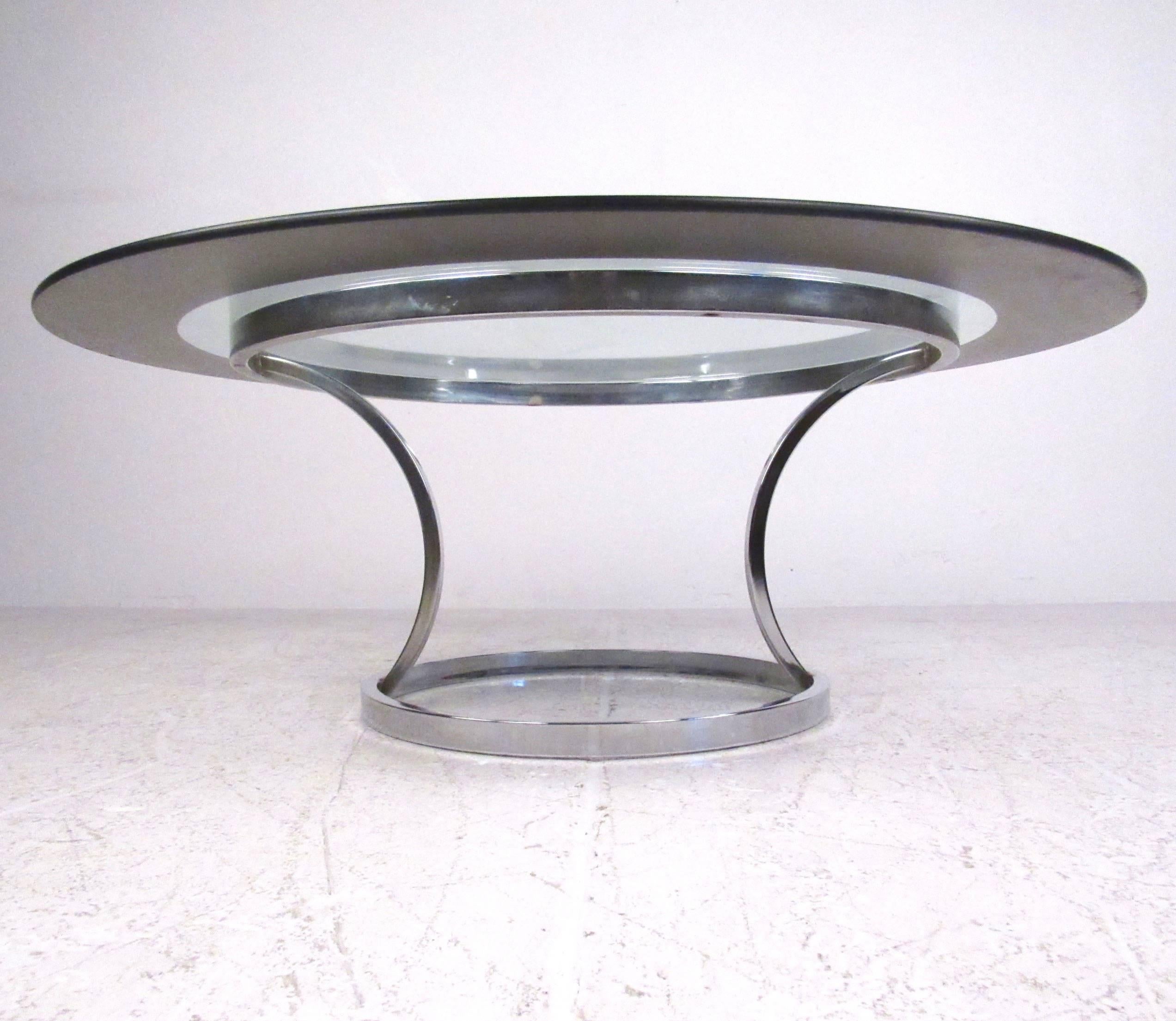 This vintage coffee table features a stylish chrome base with a circular glass top, complete with unique mirrored trim. Beautiful cocktail table from the mid-century era, this stunning modern piece makes the perfect addition to any interior. Please