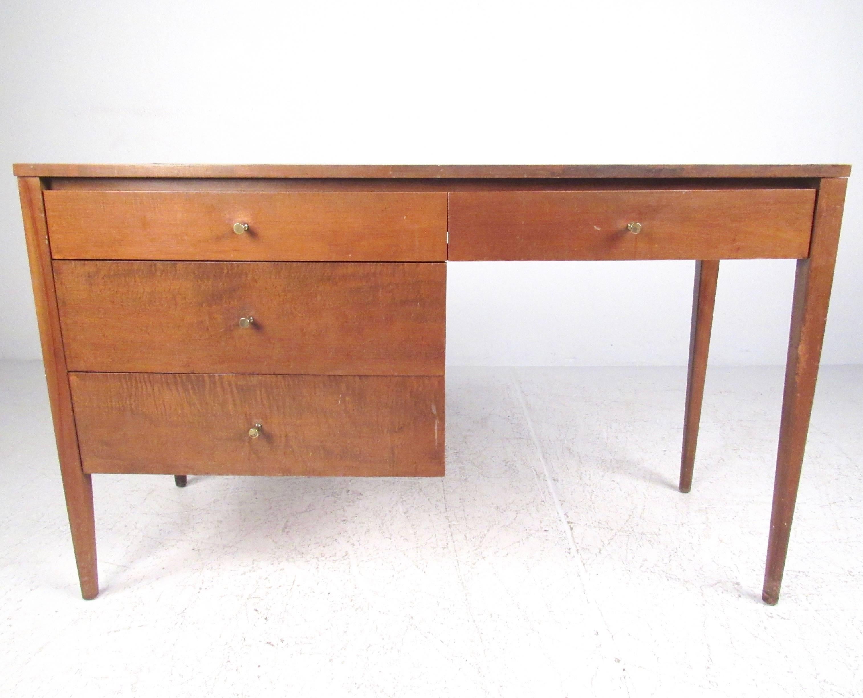 This Mid-Century Modern writing desk by Paul McCobb features a wonderful maple finish with unique brass drawer pulls. Tapered legs and spacious four drawer design make this a stylish and practical addition to home or business. Please confirm item