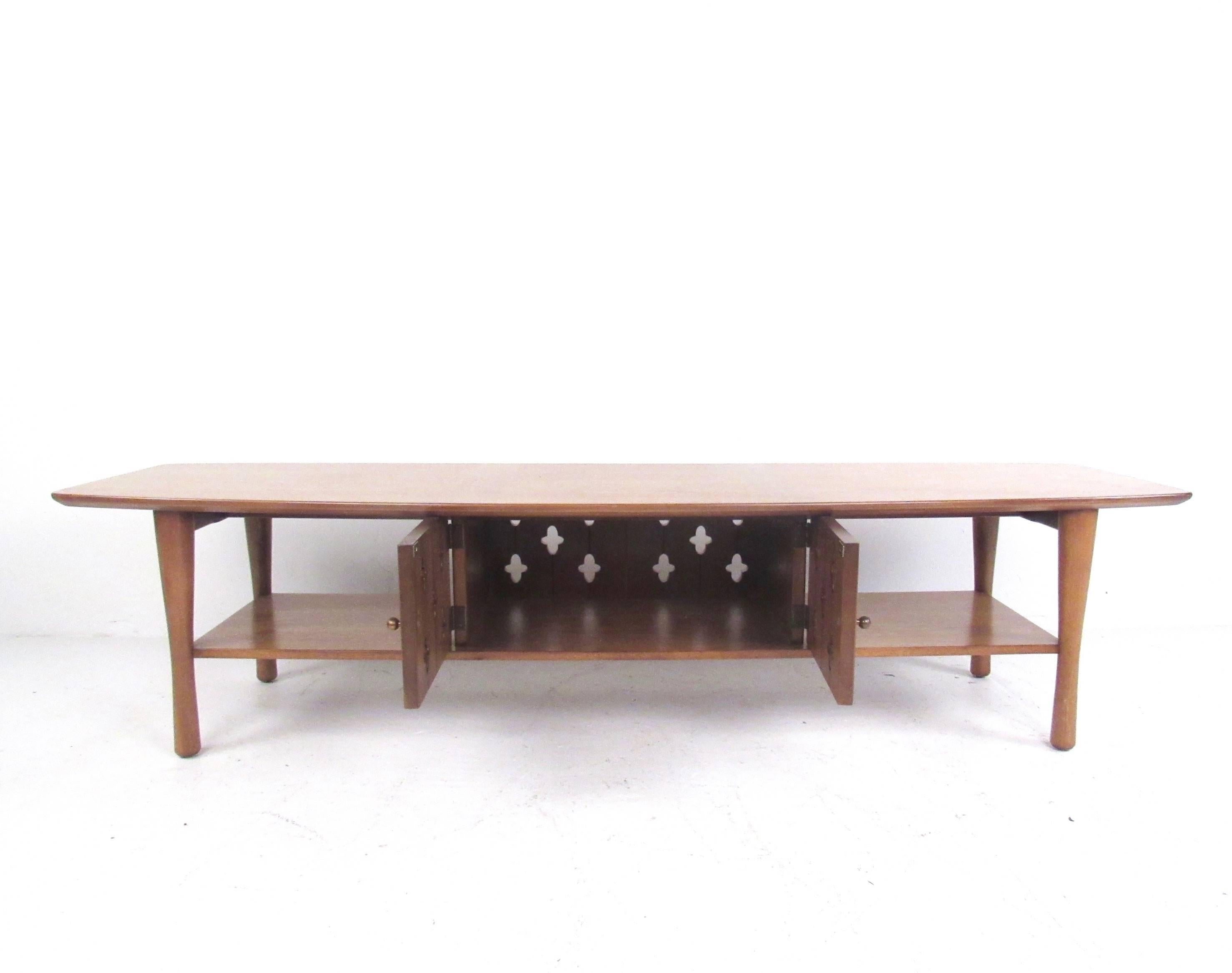 This vintage modern hardwood coffee table features a centre storage cabinet with unique cutaway design. Tapered legs and a spacious second tier for storage make this a practical yet stylish addition to any seating area. Please confirm item location