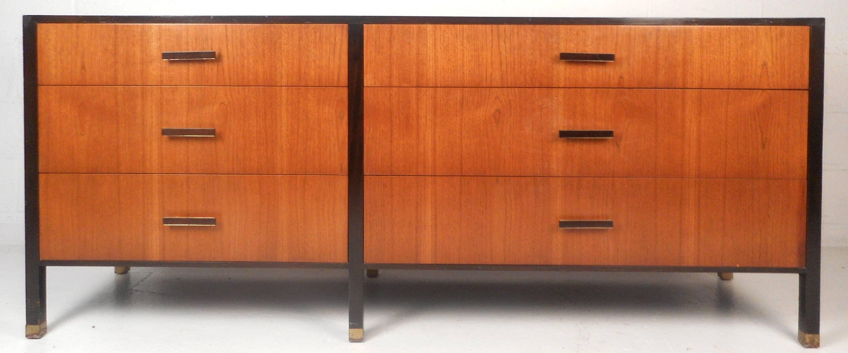 Impressive vintage modern dresser features six large drawers with unique brass and wood pulls. Stylish two-tone design has ebonized wood trim on the top and the legs. Beautiful case piece with brass capped feet offers plenty of room for storage.