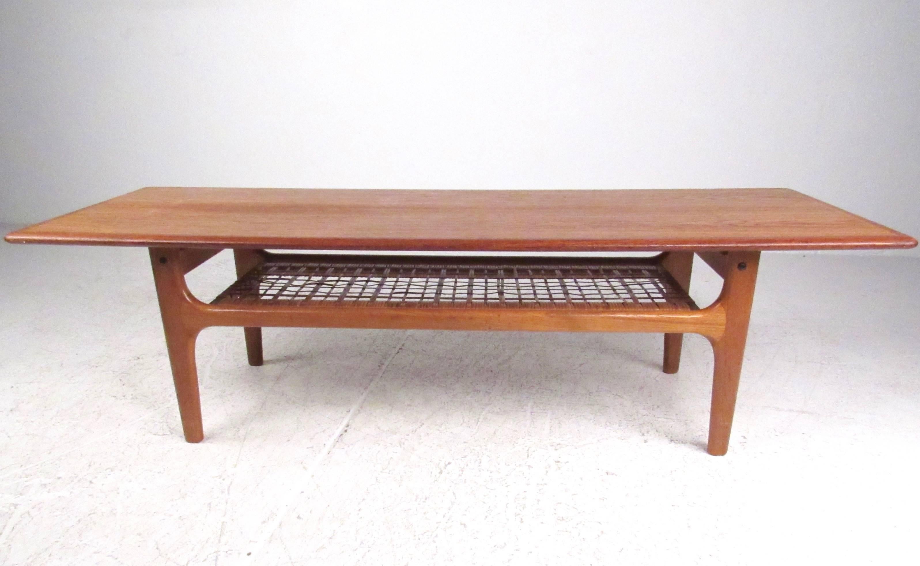 This Danish modern teak coffee table features quality Scandinavian construction with a second cane tier for added storage. This stylish vintage table is perfect for home or business use, and makes a wonderful cocktail table in any setting.