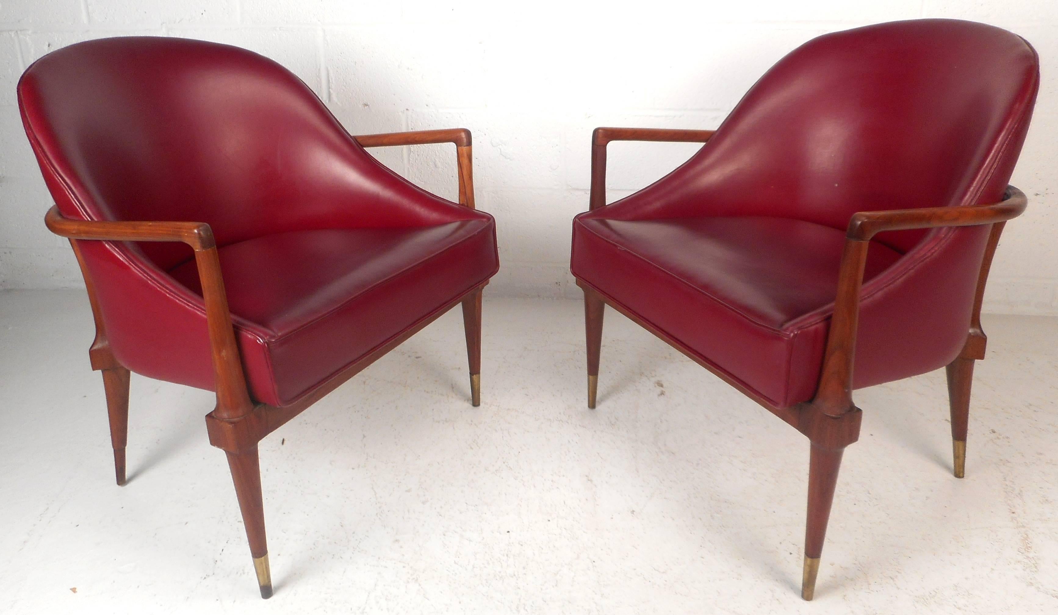 This stunning pair of vintage modern side chairs feature a solid walnut frame, brass feet, and beautiful crimson red vinyl upholstery. The stylish barrel back walnut frame wraps all the way around into unique rounded arm rests. Sculpted fixtures on