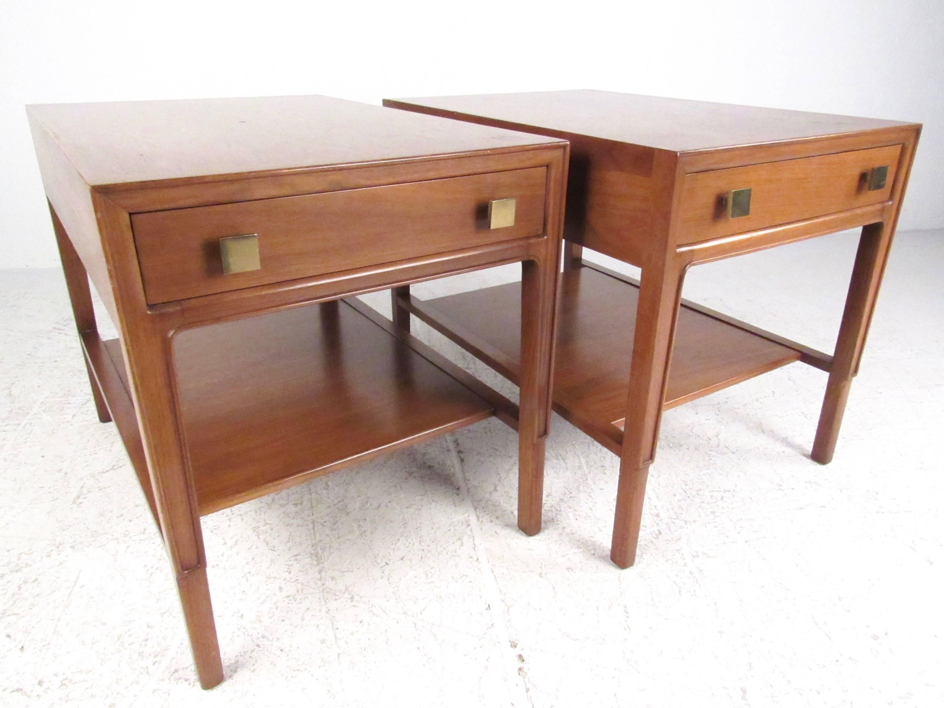 This pair of Mid-Century American two-tier nightstands by John Stuart for Mt. Airy feature a beautiful vintage finish, spacious drawers for storage and unique brass pulls. This stylish pair of "Janus" collection end tables make the perfect