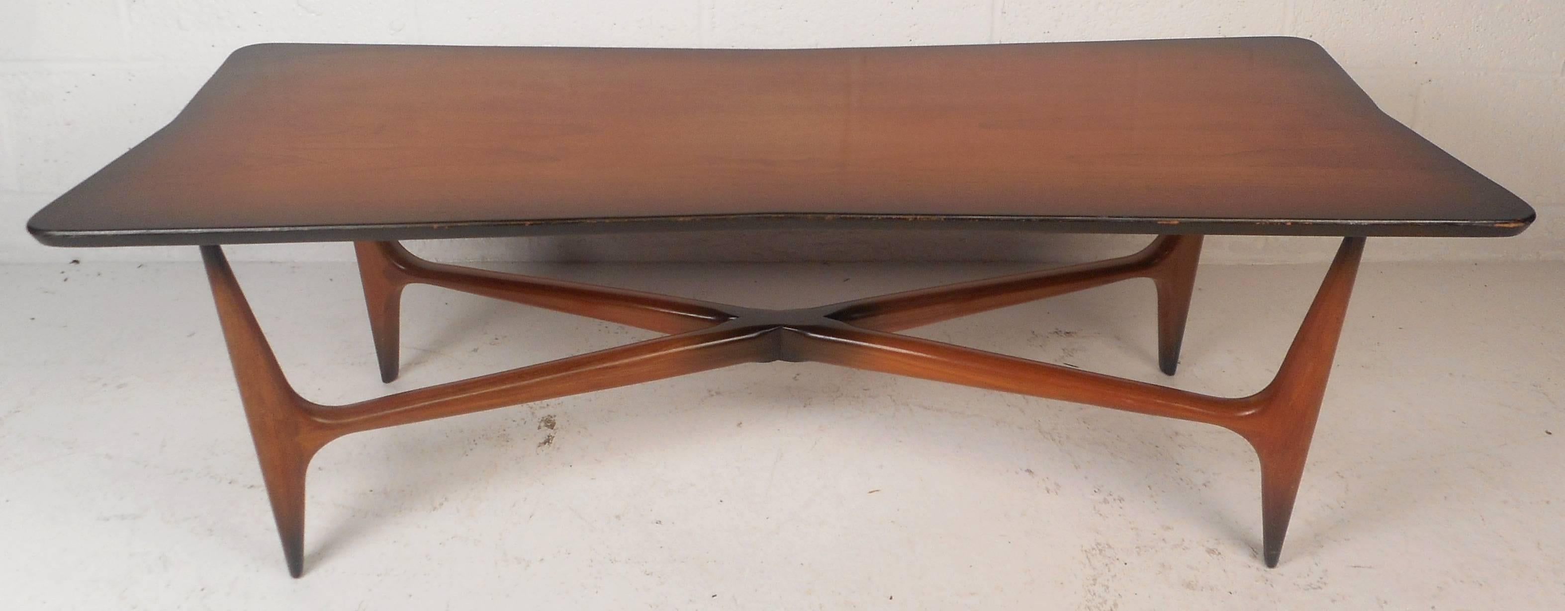 This beautiful vintage modern coffee table features a sculpted top with smooth edges. The unique design has stretchers running to each leg forming an "X" shape. The elegant shaped top sits on top of four tapered legs adding to the allure
