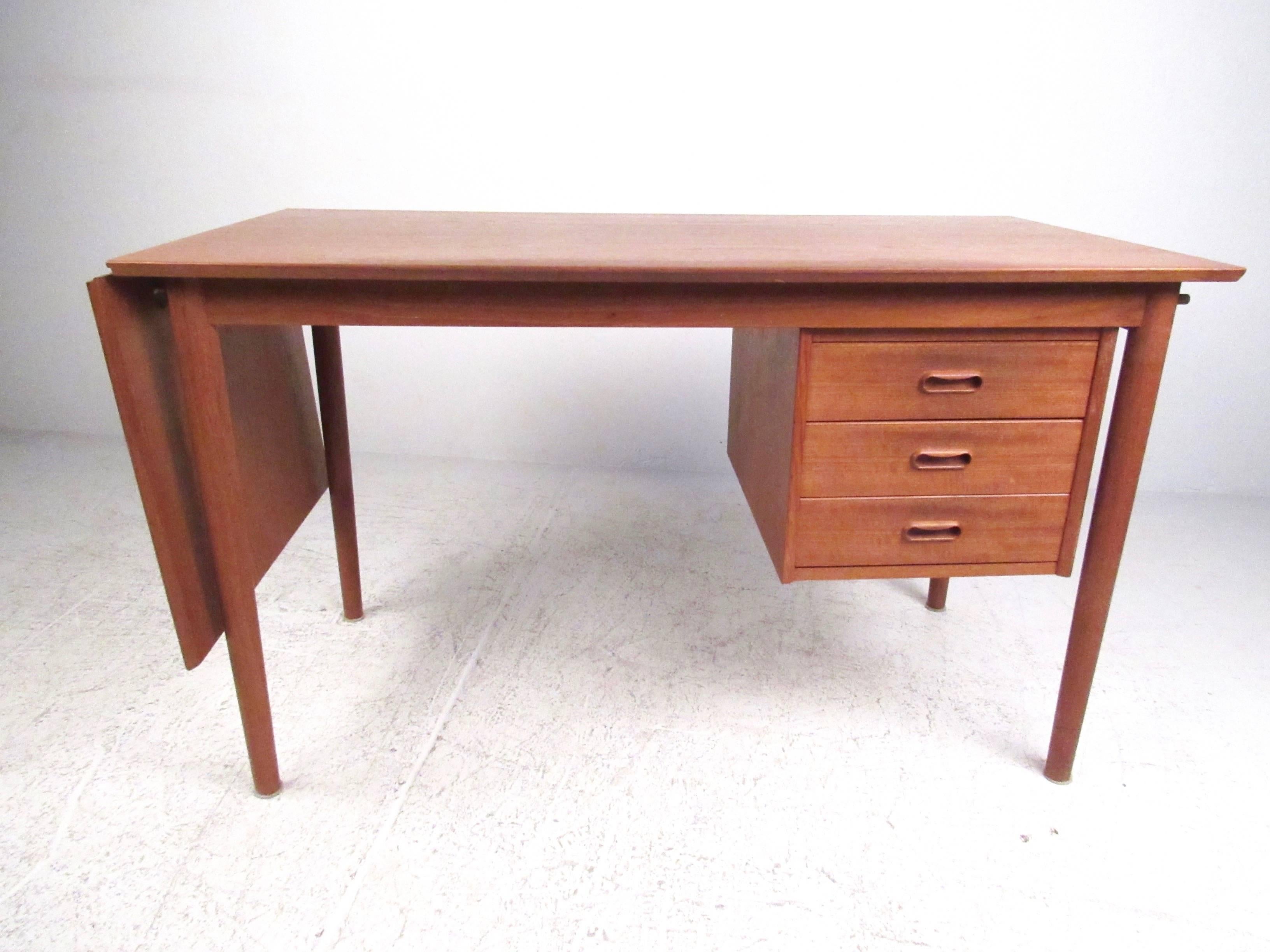 This versatile vintage teak desk features a movable three drawer cabinet that can be shifted from left to right side for customization of your layout. Perfect size for an occasional writing desk or home office, this drop leaf desk expands from 48.5'
