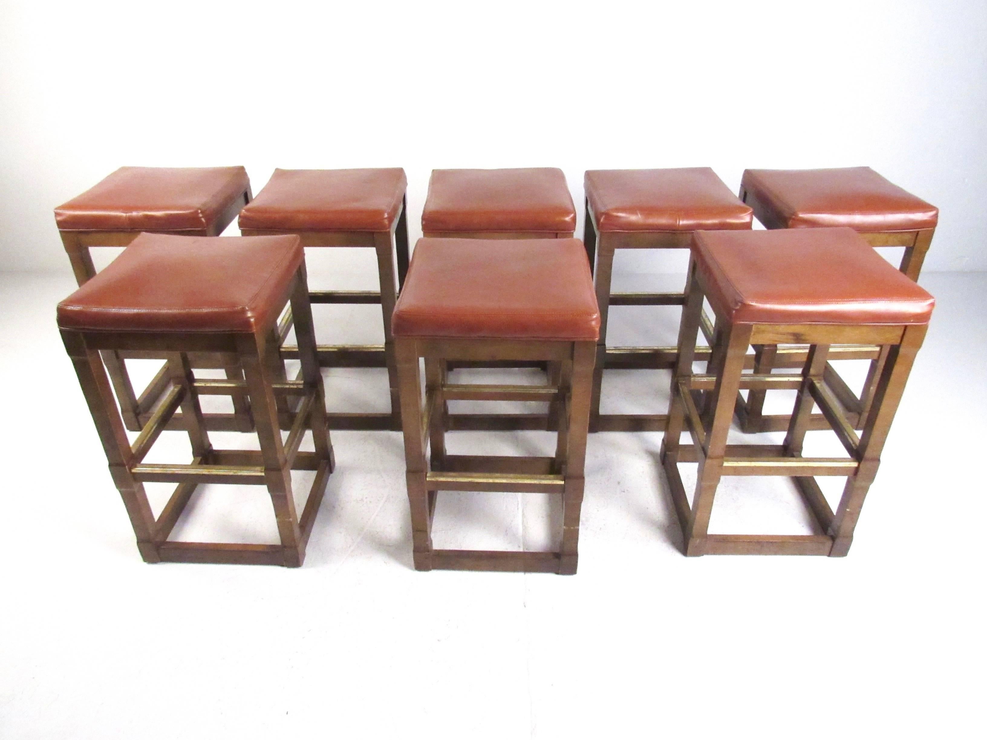 This stylish set of eight walnut counter stools feature sturdy square bases with upholstered vinyl tops. Brass trim on stretchers and tapered frame add to the vintage charm of the set, ideal for home or business counter seating. Please confirm item