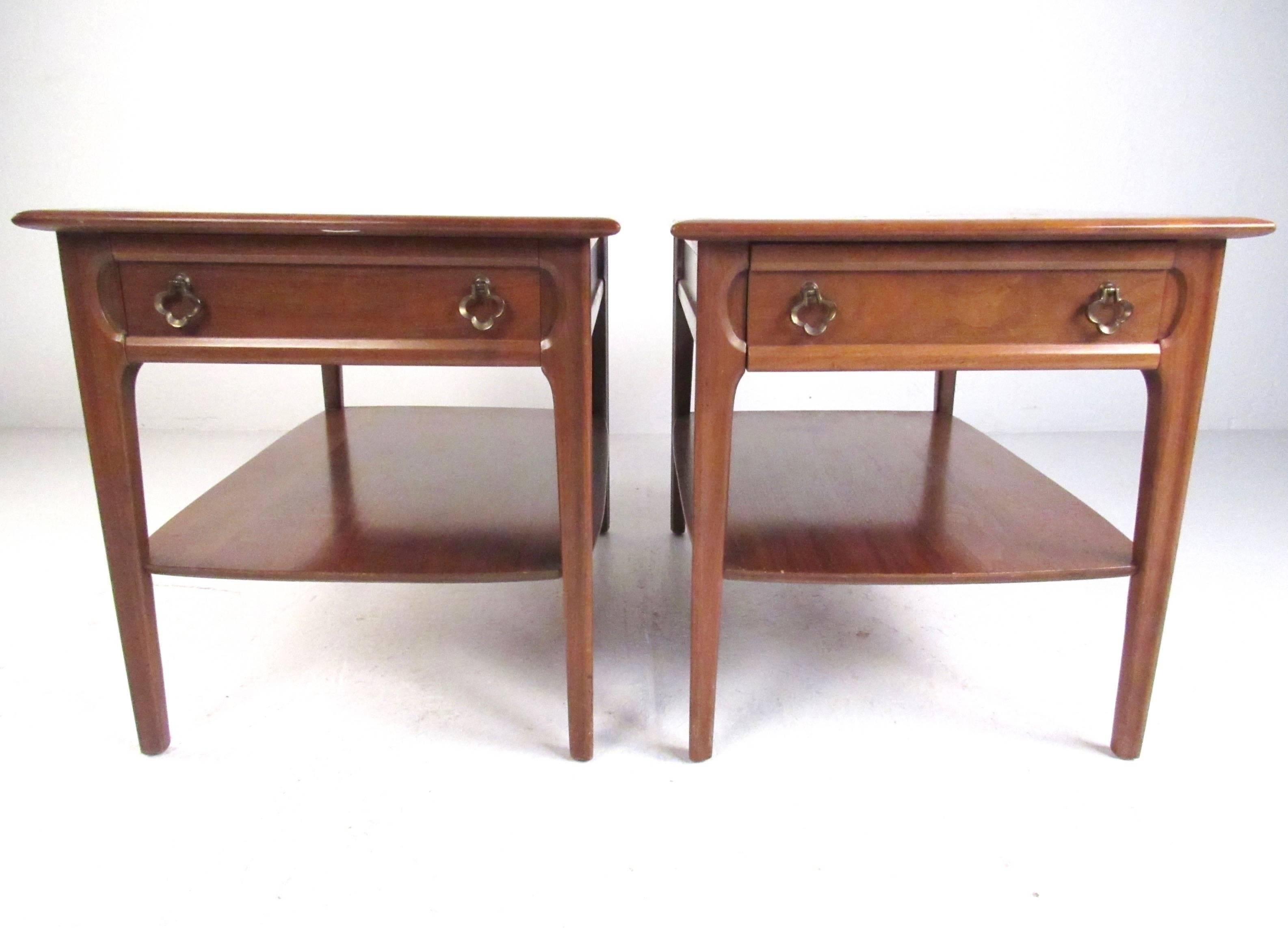 This stylish pair of walnut side tables feature uniquely sculpted accents, dual-tier construction and ornate brass pulls. Perfect matching set to add Mid-Century style and spacious storage to any interior setting from sofa side table to bedside