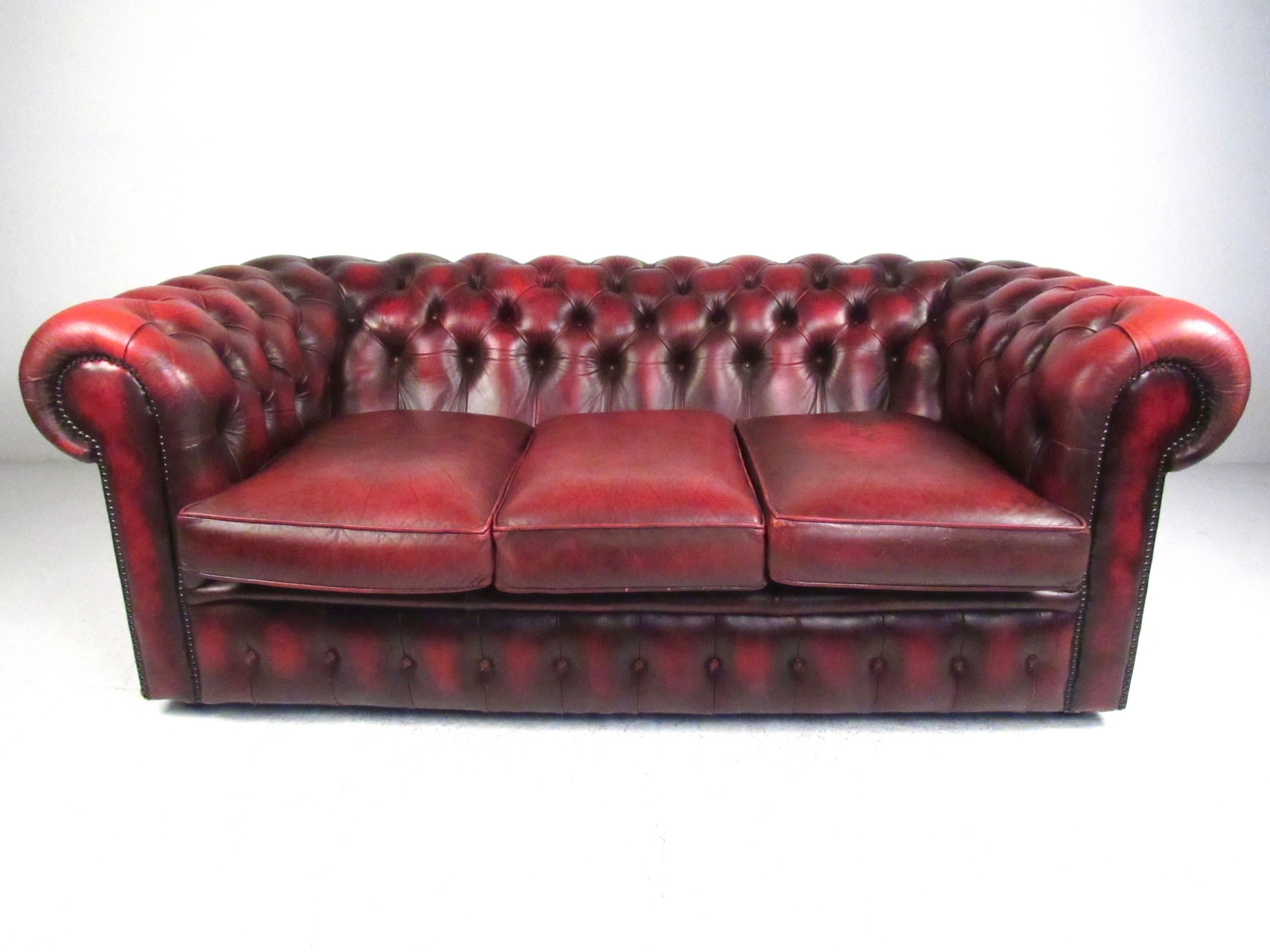 This stylish vintage Chesterfield features rich tufted leather with a unique patina from time and use. This impressive sofa features elegant scrolled arms and comfortable three-seat configuration, making a perfect addition to home or business.