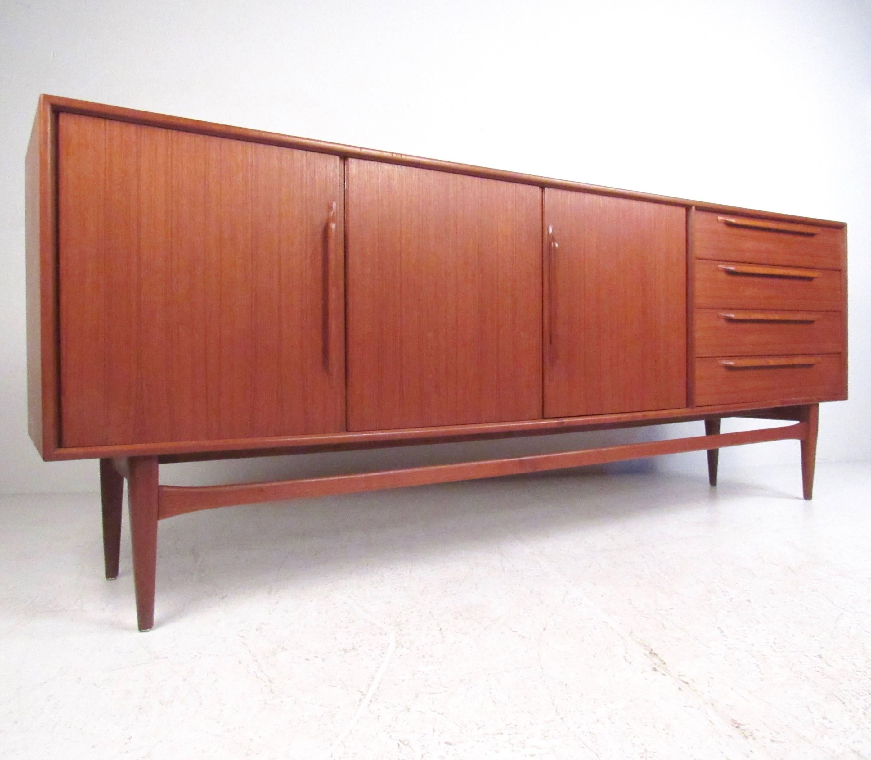 This exquisite vintage teak sideboard features elegant sculpted pulls, tapered legs and shapely leg stretcher for addition support. Spacious interior cabinet offers adjustable shelf storage, while four hardwood drawers make it easy to organize in