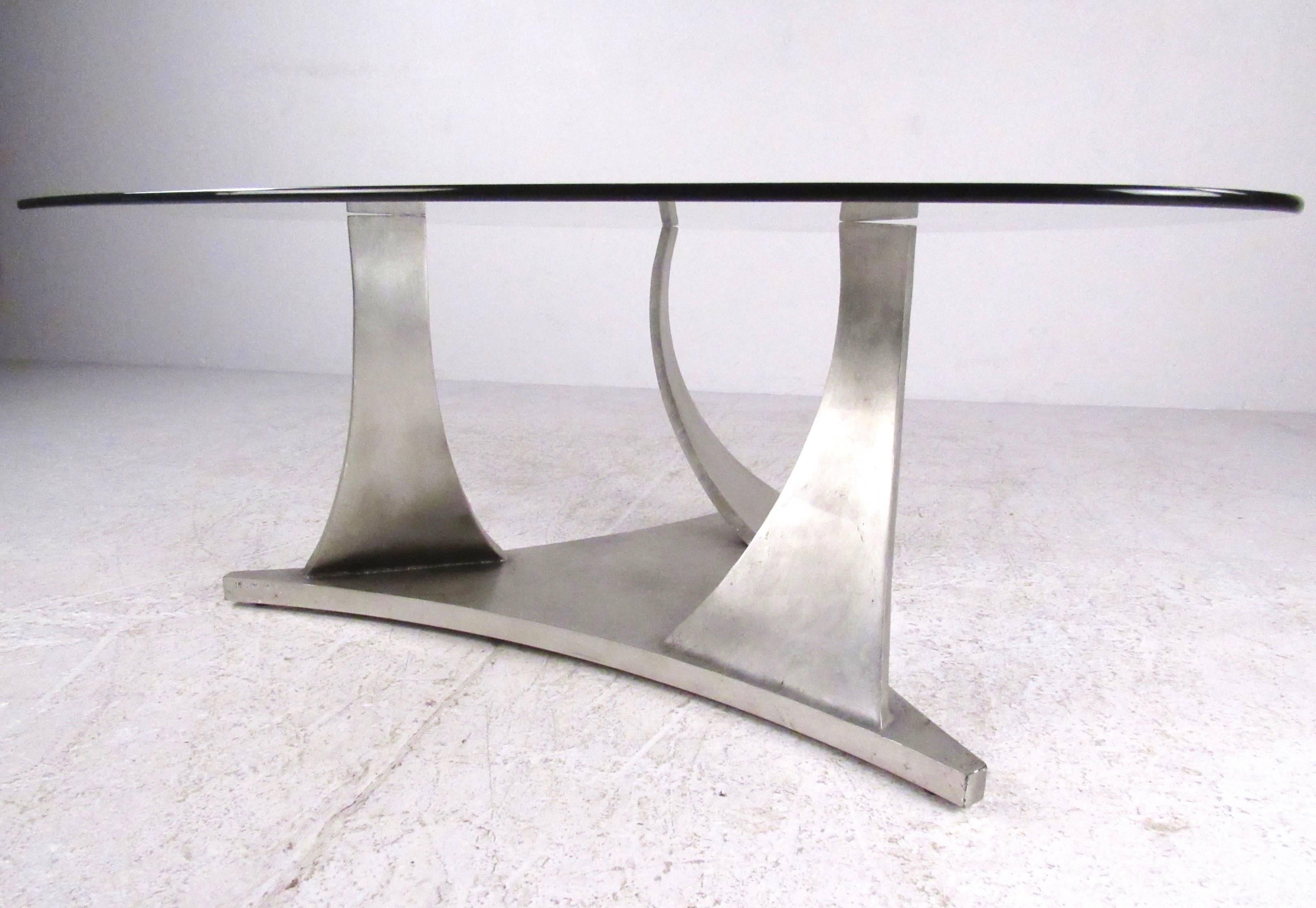 This stylish modern cocktail table features sculpted metal base and unique triangular style glass top. This substantial metal base features a metallic color paint job, while the proportions and impressive size make this a wonderful centre table in