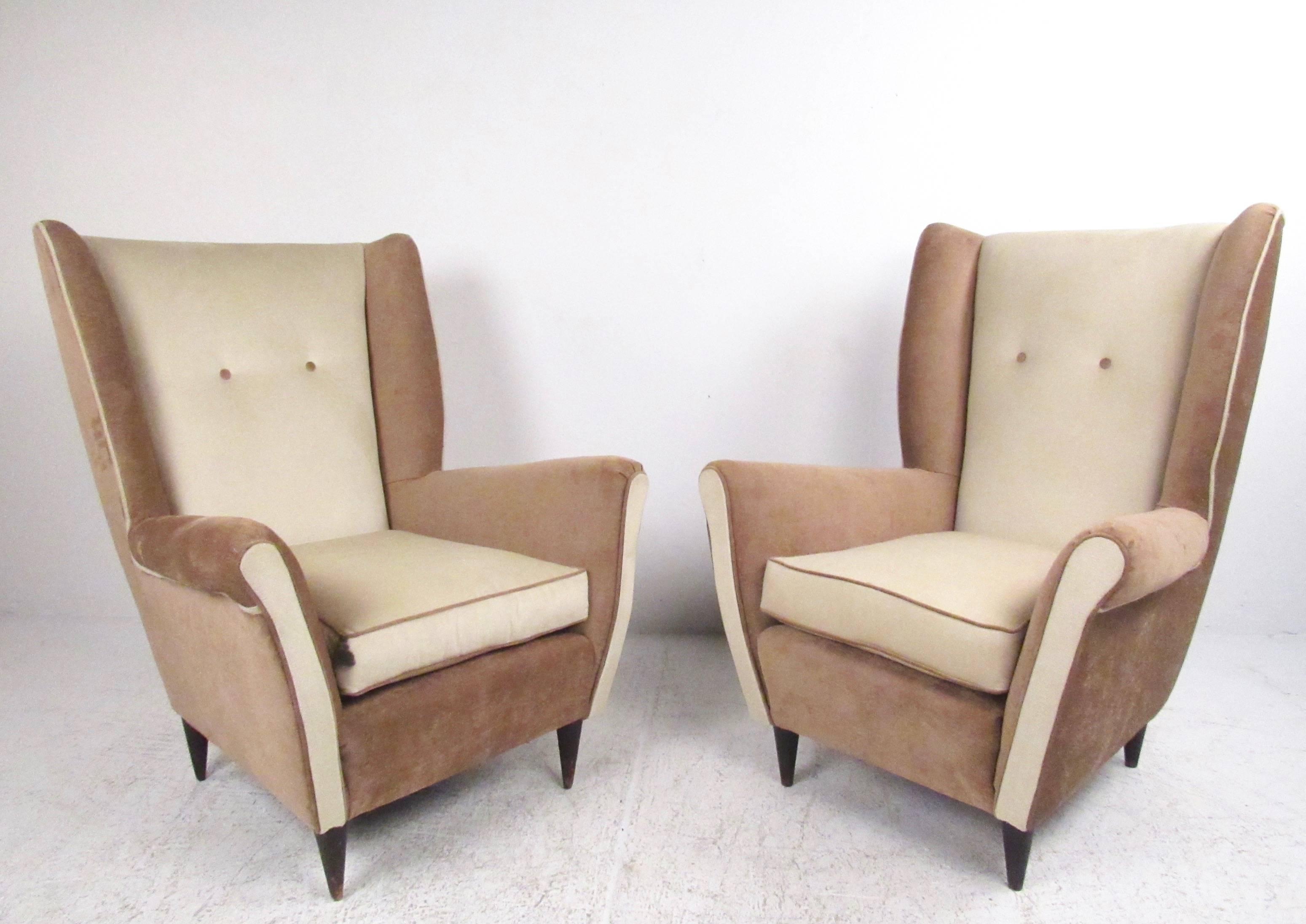 This stylish pair of Mid-Century lounge chairs feature high sculpted seat backs, comfortable and accommodating seats and tapered hardwood legs. Exquisite two tone fabric is complimented by trim piping and button tufted seat backs. Perfect pair of