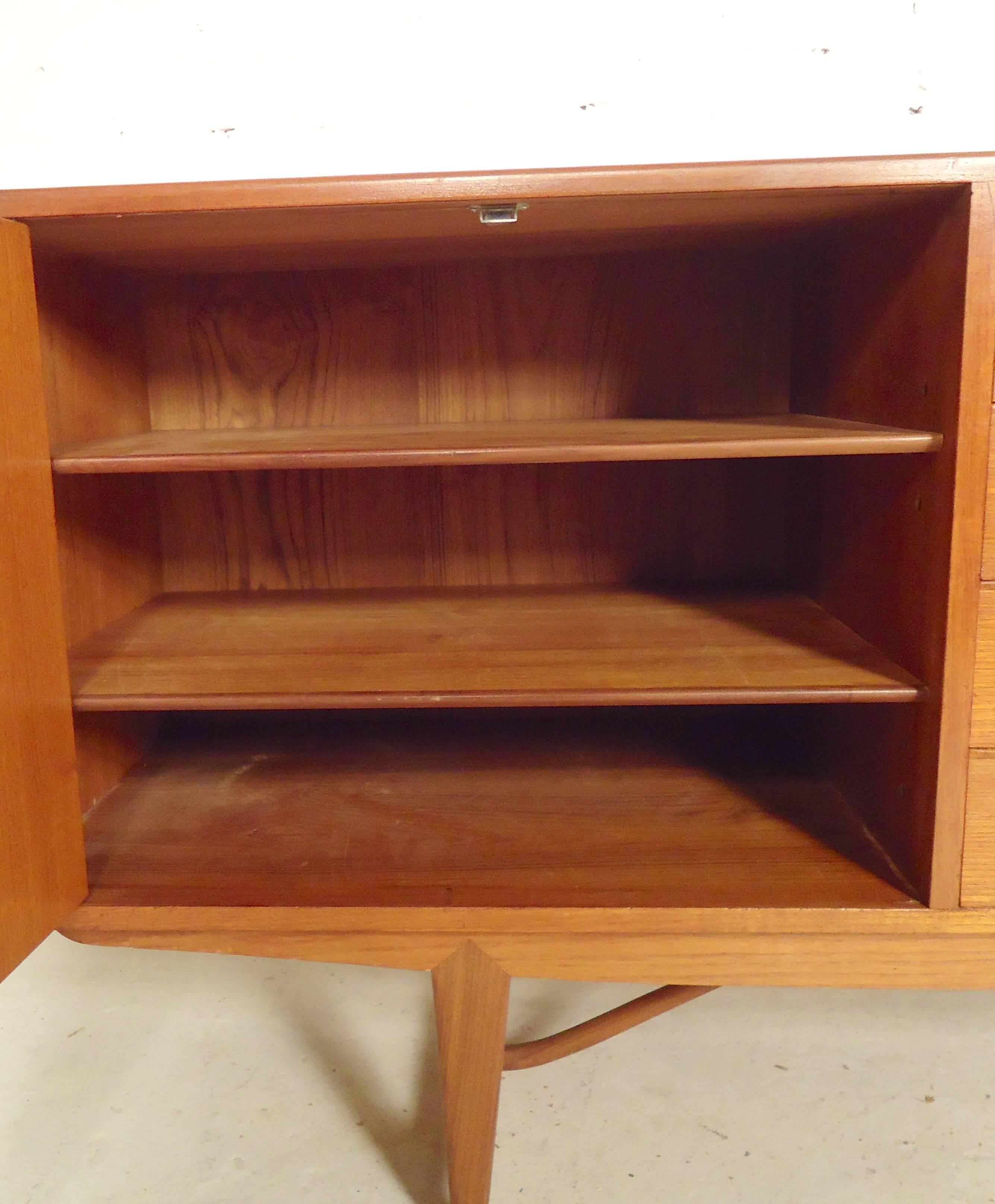 Very rare and unusual sideboard in warm teak grain. Featuring five middle drawers and two bi-fold cabinet doors, all with finely sculpted handles.

(Please confirm item location - NY or NJ - with dealer).
 