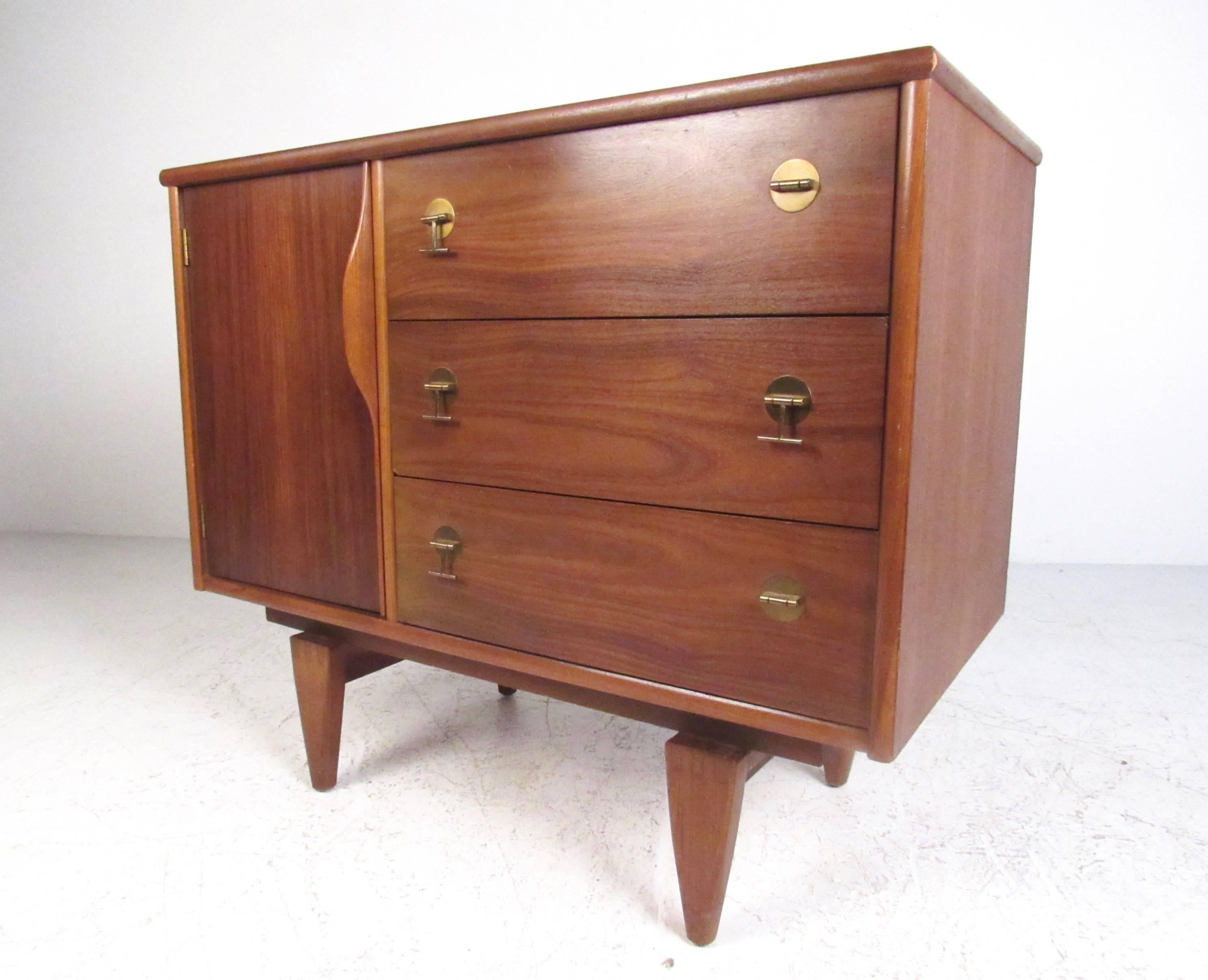 This stylish vintage walnut cabinet by Stanley furniture features sculpted hardwood handle, unique brass pulls, and tapered dovetail legs. Unique Mid-Century Modern style and pull-out shelved cabinet space make this a beautiful addition to home or