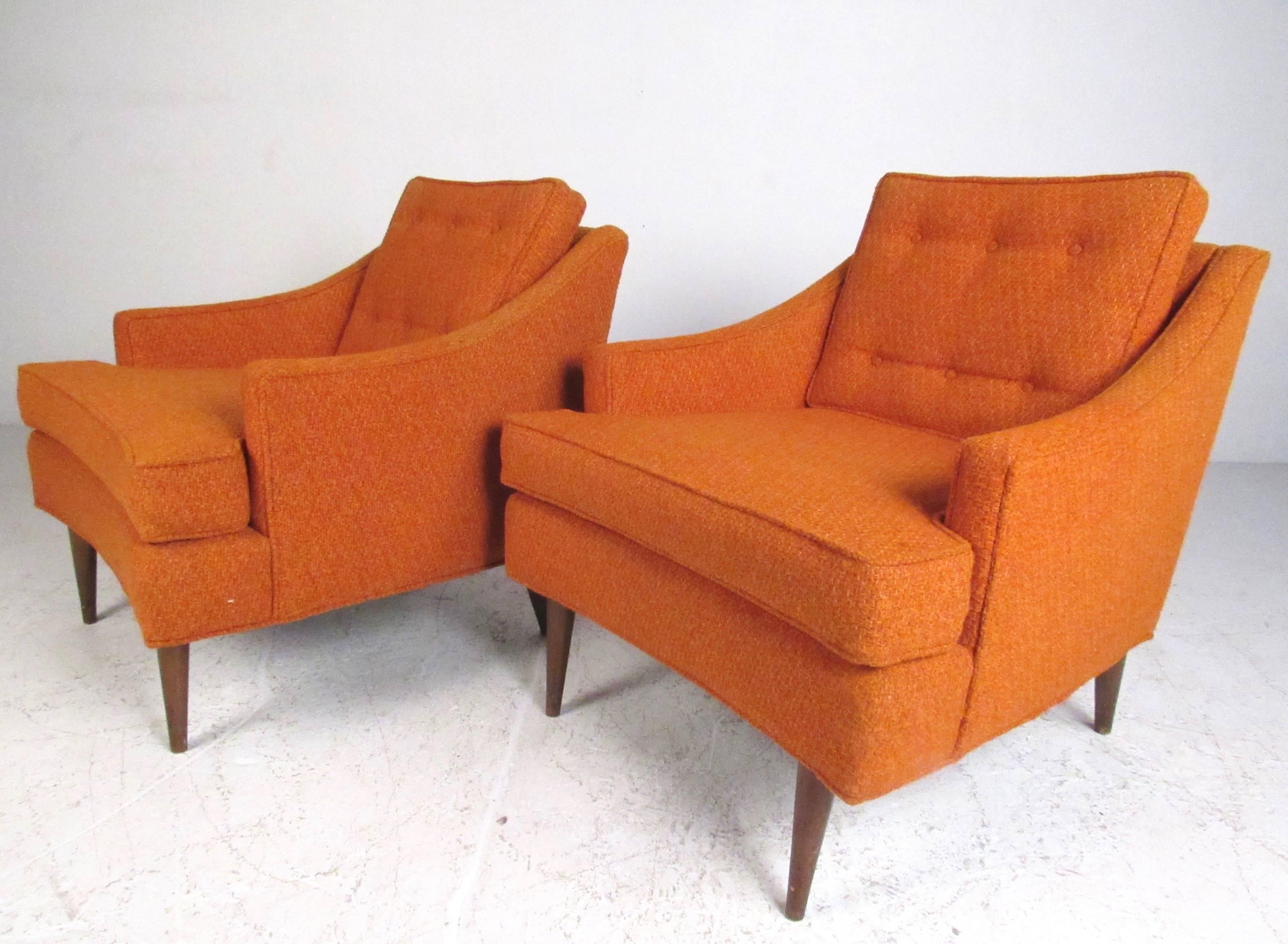 This matching pair of vintage lounge chairs feature comfortable upholstered frames with tapered walnut legs and tufted cushions. Sleek sloped arm rests add to comfort and style of the pair. Please confirm item location (NY or NJ).