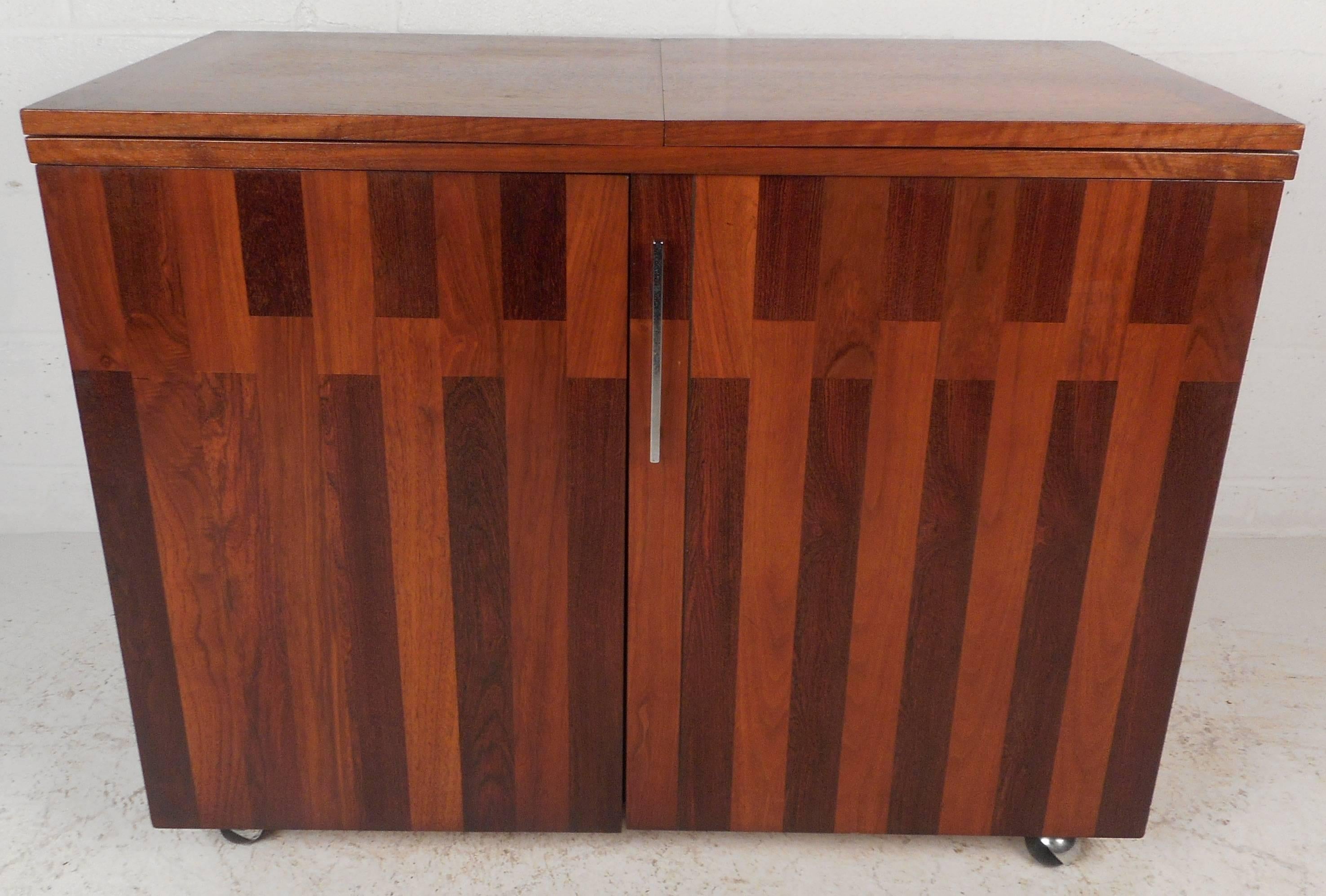 Beautiful vintage modern rolling bar with a unique walnut and rosewood front. Elegant design features a flip-top that opens all the way up to 76 inches wide. Rosewood strips on the top edges and a finished back add to the allure. Two cabinet doors