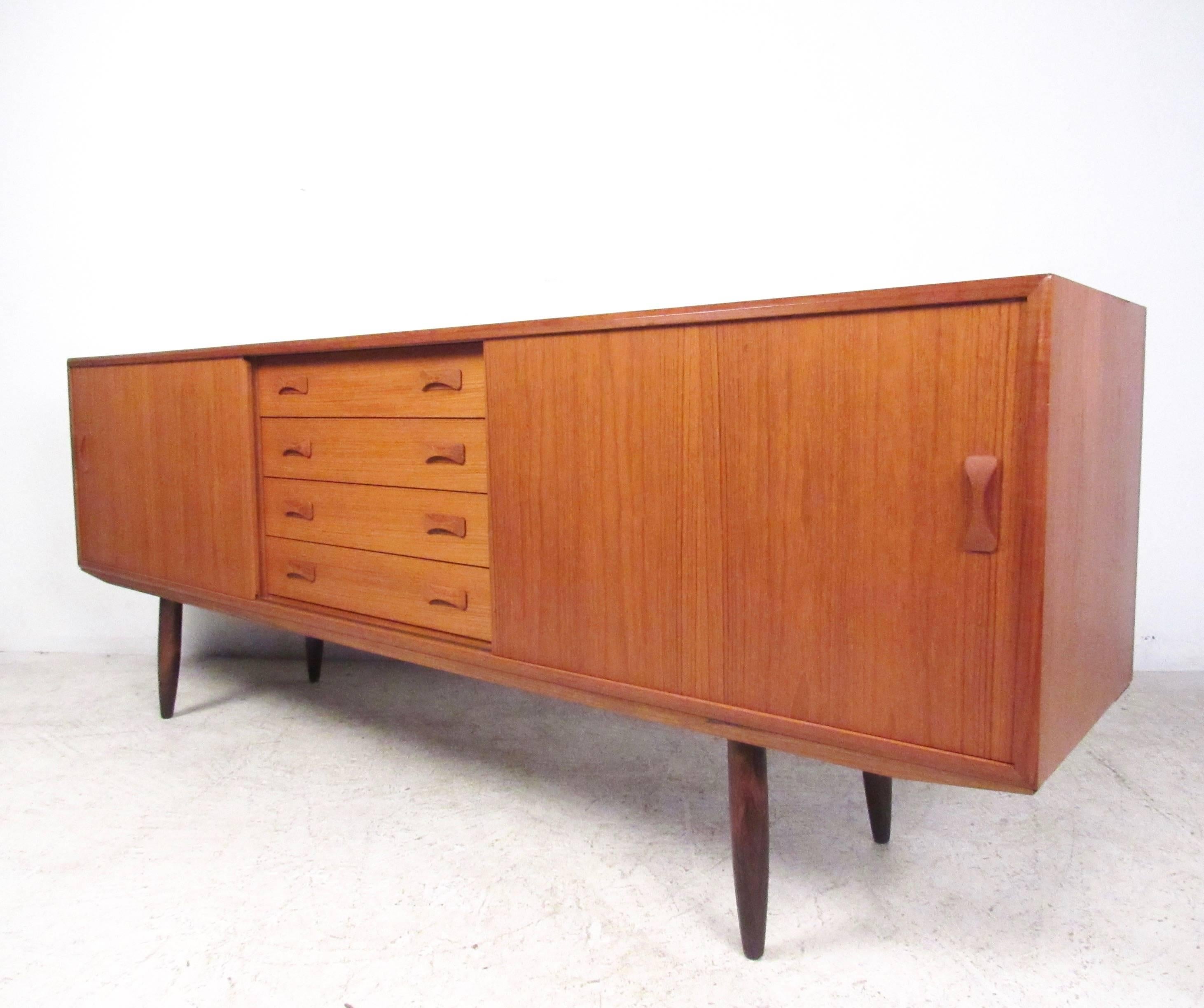 This stylish teak sideboard features quality mid-century construction including dovetail drawers, carved pulls, and rich teak finish. Tapered legs and spacious storage cabinets add to the Scandinavian modern charm of the piece, which makes an