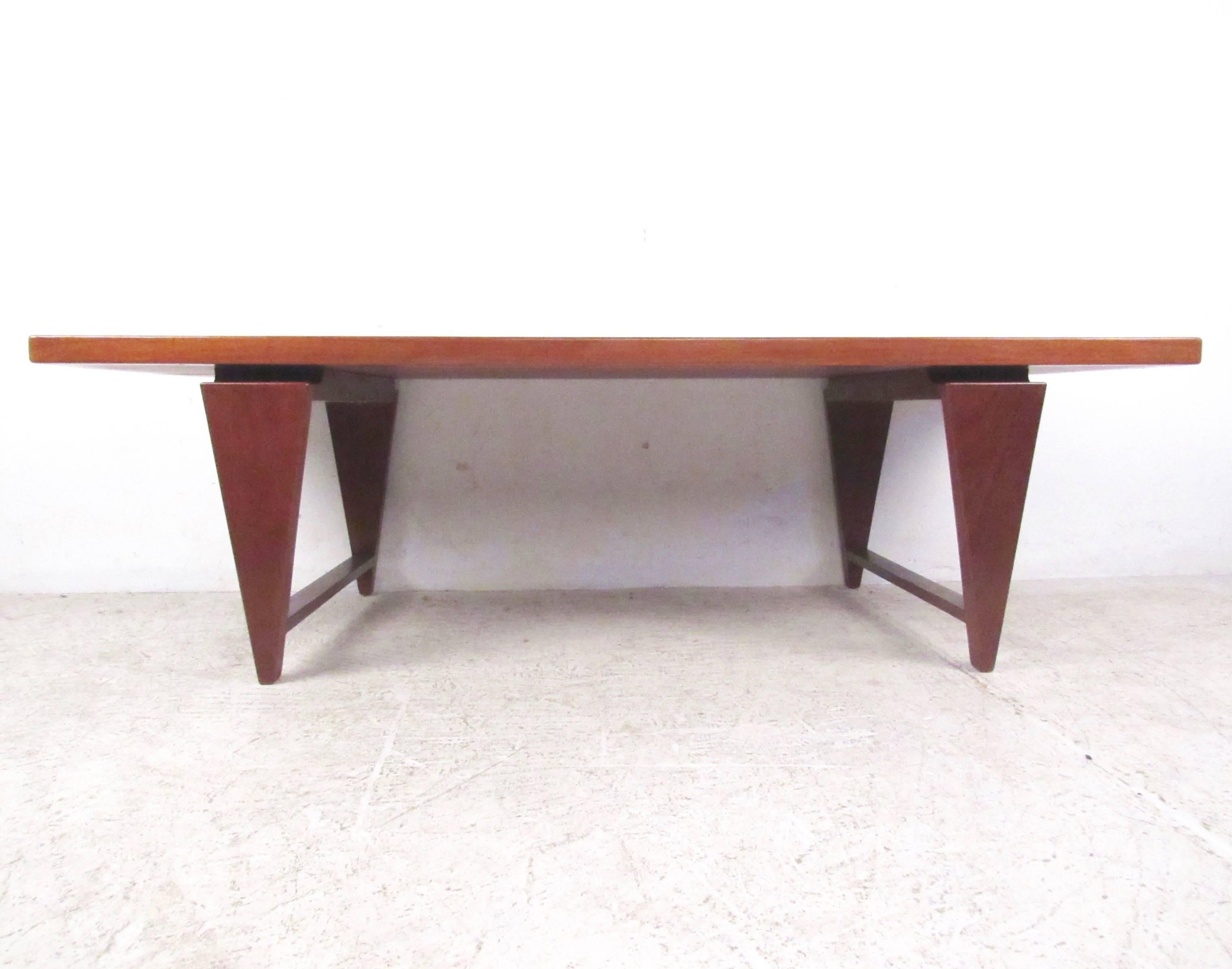 This unique vintage modern coffee table boasts triangular legs connected by stretchers ensuring maximum sturdiness. A sleek design by Illum Wikkelso with a large rectangular table top and elegant teak wood grain throughout. This well constructed