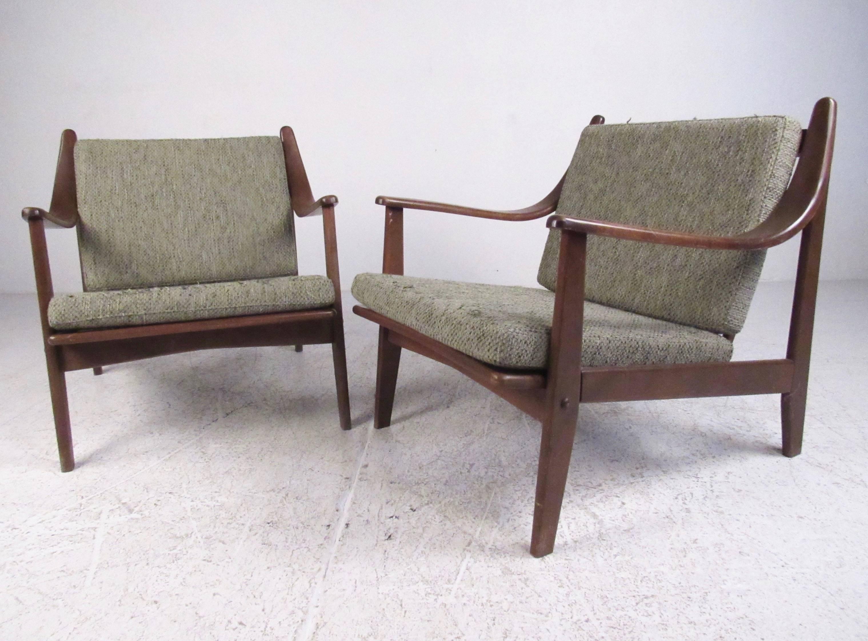 This stylish pair of Mid-Century Modern lounge chairs feature sculpted walnut construction with comfortable vintage upholstery. Spingle backs and unique sloped arm rests add to the Danish modern Finn Juhl style of the pair. Please confirm item