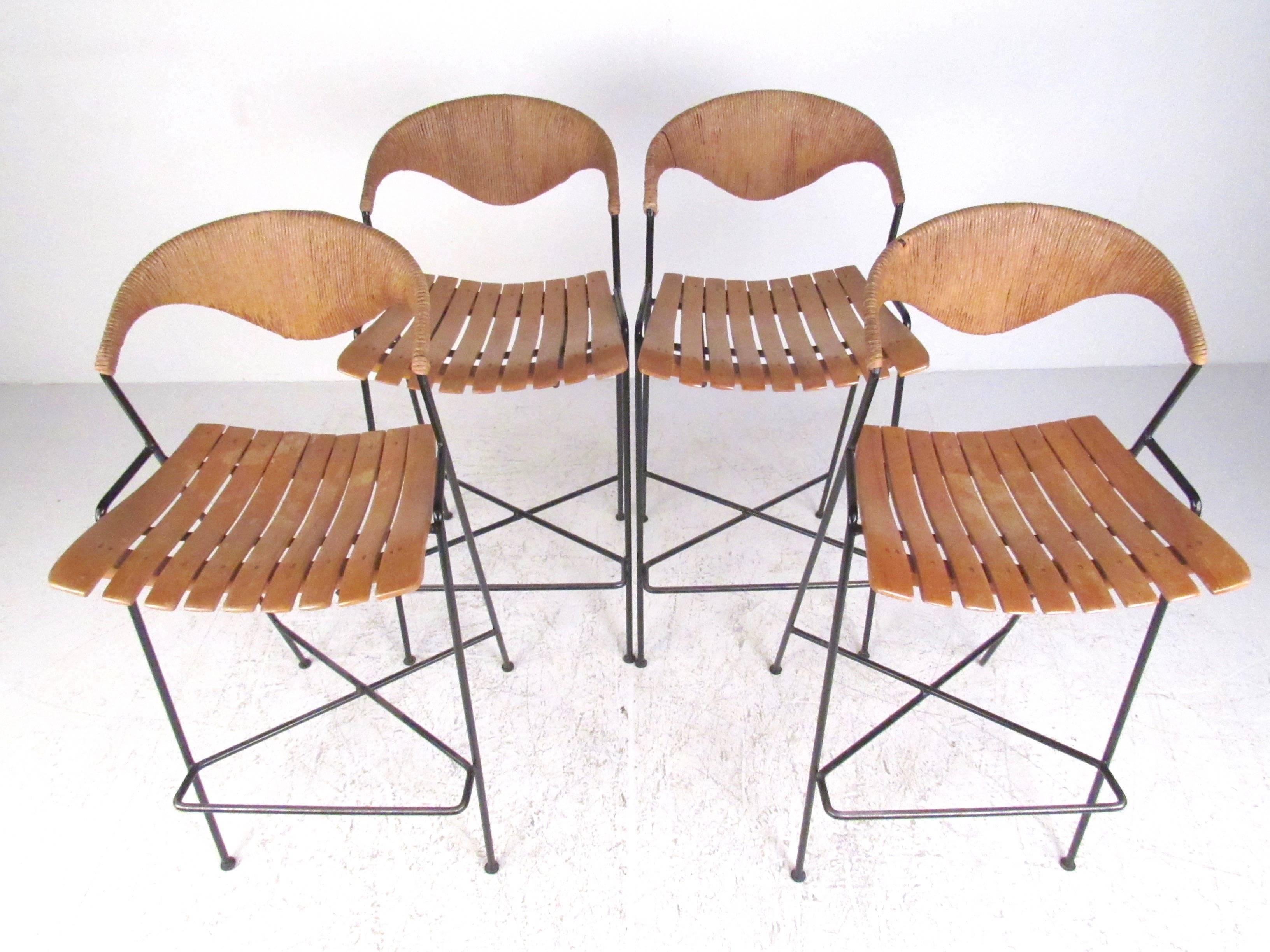 This stylish set of four Mid-Century bar stools feature slat seats and unique rush covered seat backs. Sculptural Arthur Umanoff design combines cast iron frames with natural seating materials for an organic modern appeal. Perfect addition to home