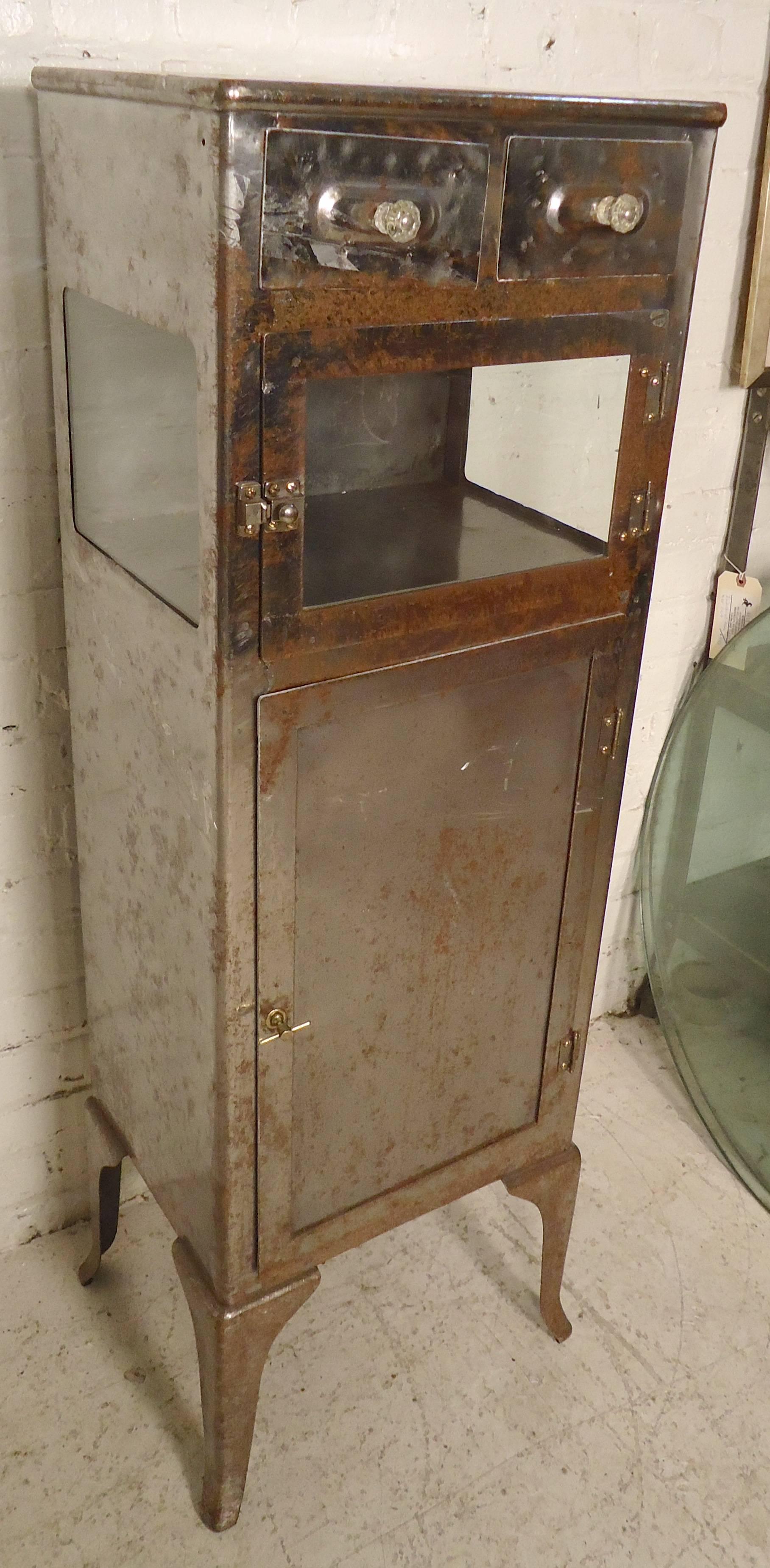 Petite metal cabinet perfect for bathroom storage. Two cabinet spaces, one with glass front and sides. Piece has been refinished in a bare metal style.

(Please confirm item location NY or NJ with dealer).
  