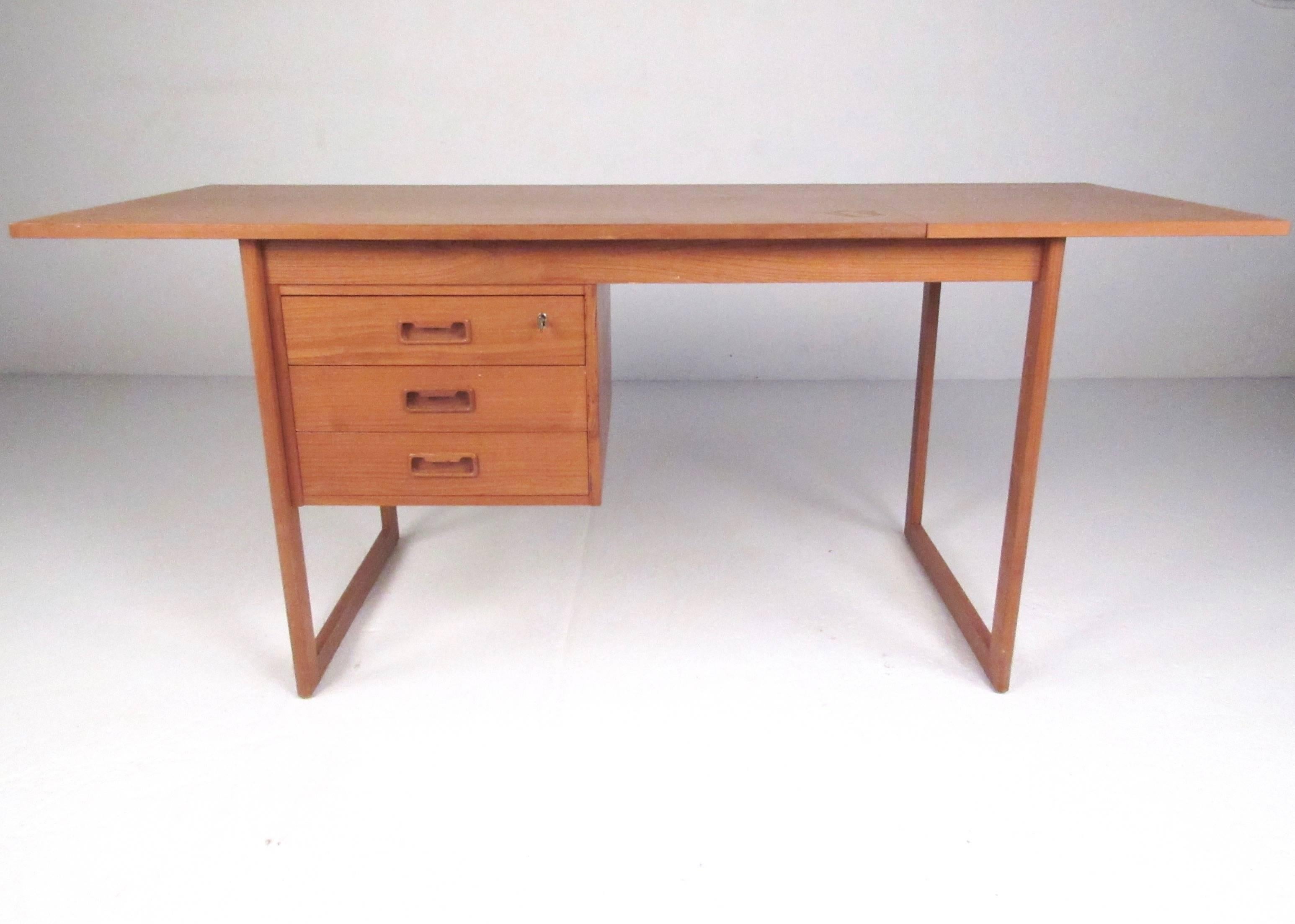 This beautiful Mid-Century Modern writing desk features stylish sled legs, locking drawers, and Danish teak construction. Unique Arne Vodder style drop-leaf extensions takes this desk from a width of 48 inches to 66.5 inches. Please confirm item