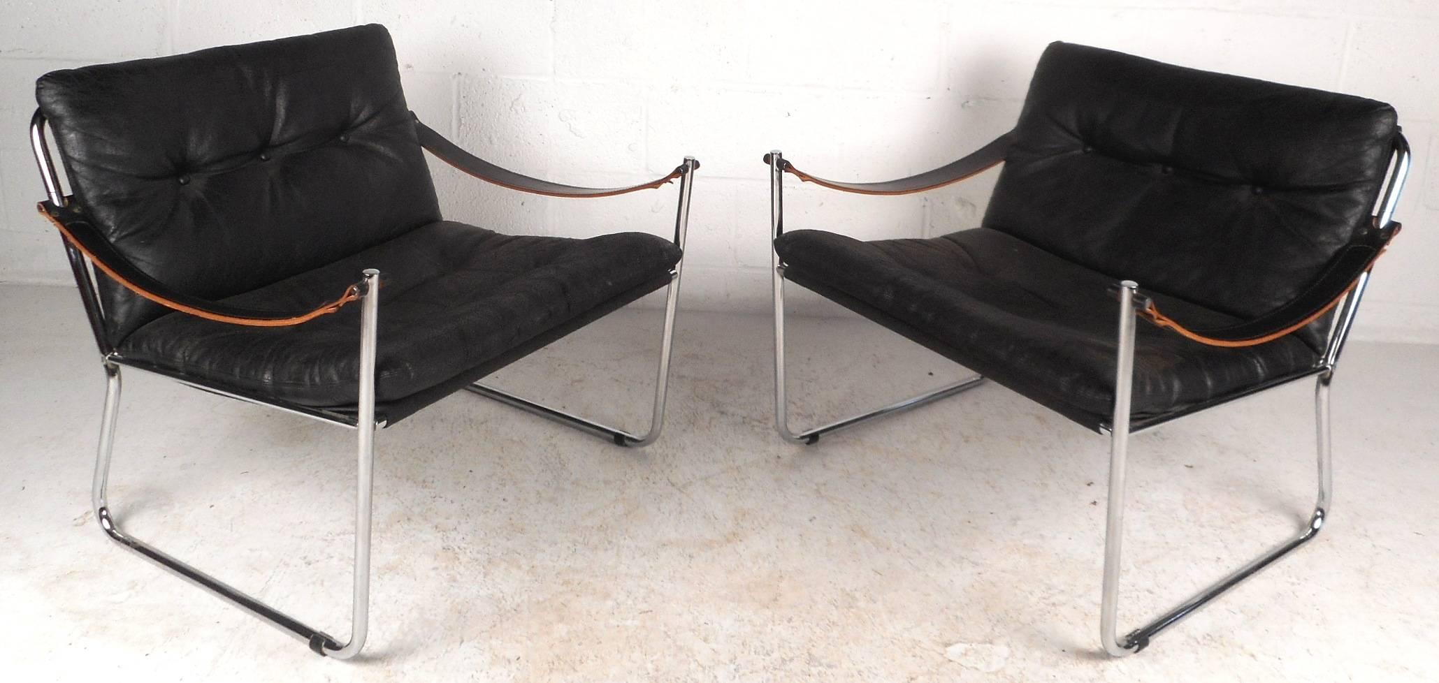 This beautiful pair of vintage modern wide lounge chairs feature thick leather straps that function as arm rests and a thick tubular chrome-plated frame. Sleek design with a thick padded cushion covered in tufted vinyl upholstery. The Angled sled