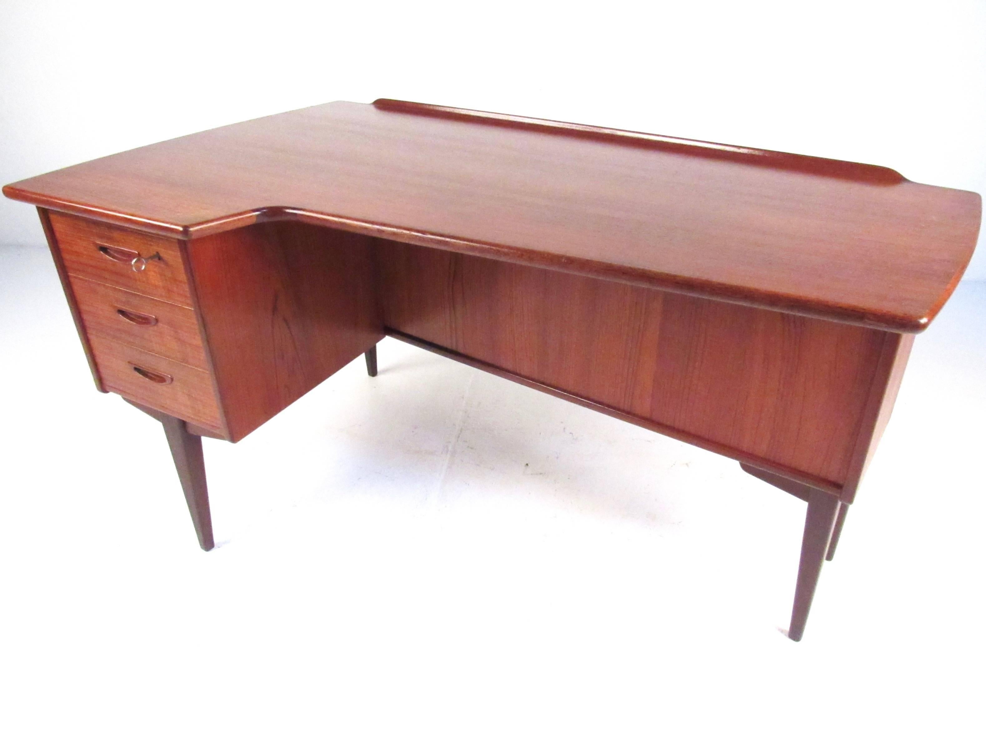 This stylish Mid-Century Danish teak desk by Peter Lovig Nielsen features a rich vintage finish, raised back edge, and double sided design. Dovetailed locking drawers, drop down cabinet storage, and tapered legs add to the Scandinavian Modern design