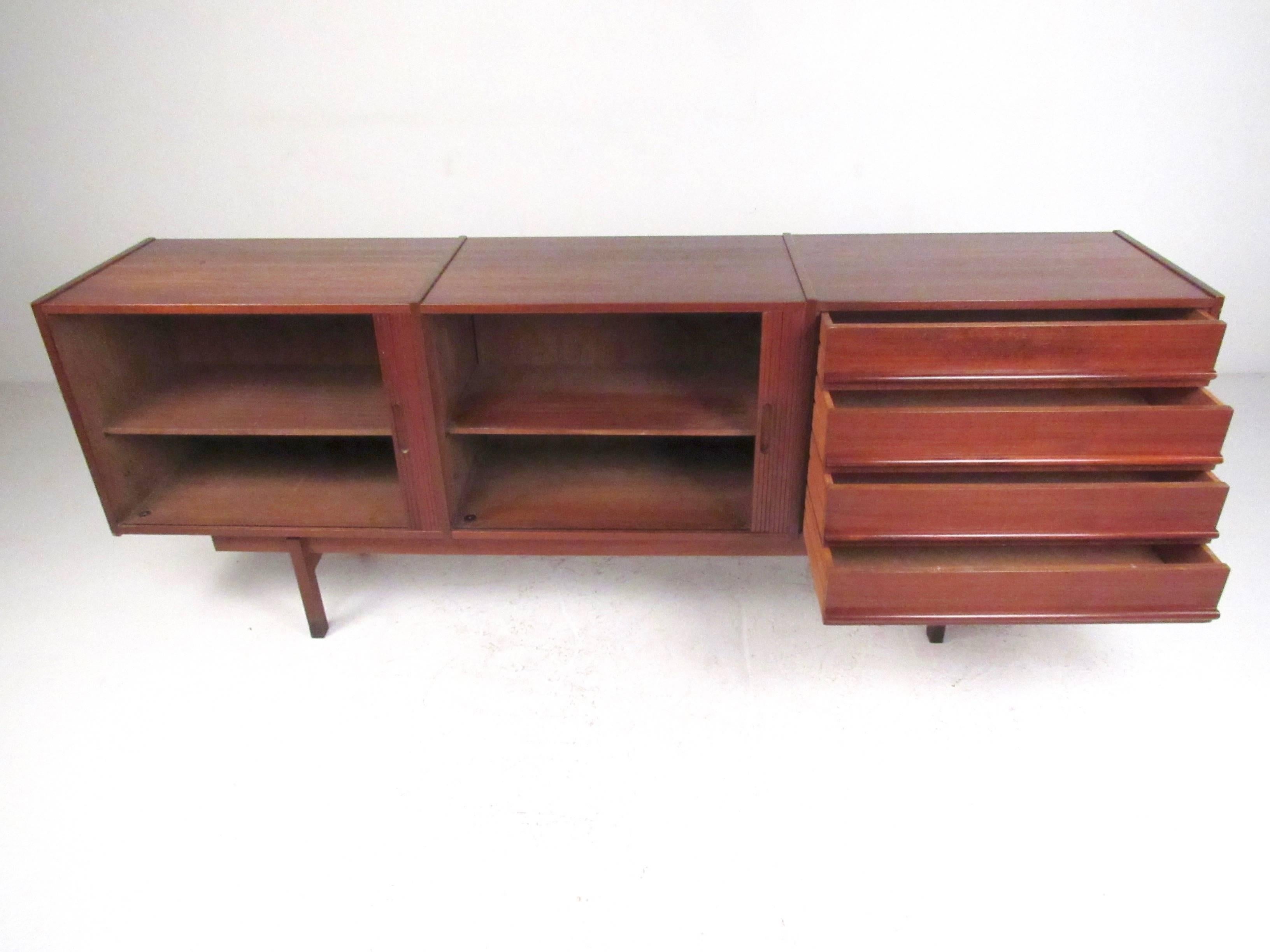 This stylish vintage teak sideboard features unique side by side tambour cabinets and four wide drawers for extra storage. The unique layout of this Mid-Century sideboard shows signs of quality 1950s construction, with raised top and shapely modern