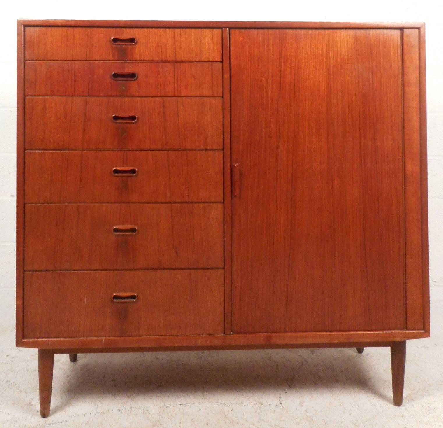 This gorgeous vintage modern gentleman's chest features an abundance of storage space within its 12 hefty drawers. Sleek design has unique carved pulls on six of its drawers and a tambour door that slides open to unveil six more drawers. Impressive