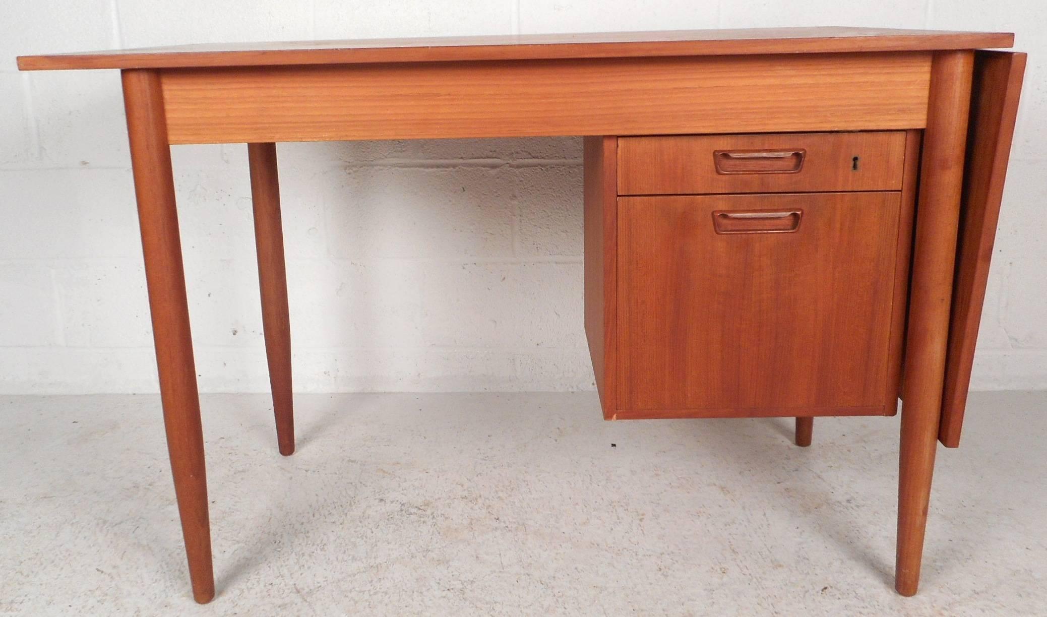 Stunning vintage modern desk features the unique ability to extend the width of the top by sliding it to the side. Beautiful teak wood grain, long tapered legs, and a finished back show quality craftsmanship. This sleek and functional Mid-Century