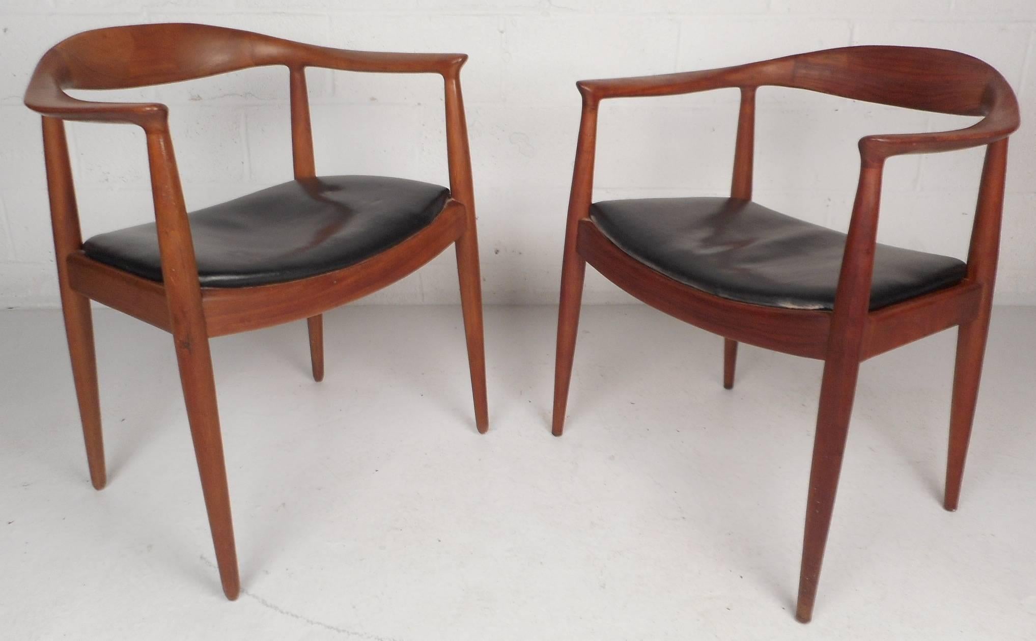 This stunning pair of vintage modern side chairs feature sculpted arm rests and a unique barrel backrest. Elegant wood grain compliments the black leather seats. Sleek design sits on top of four long angled and tapered legs which provide sturdiness