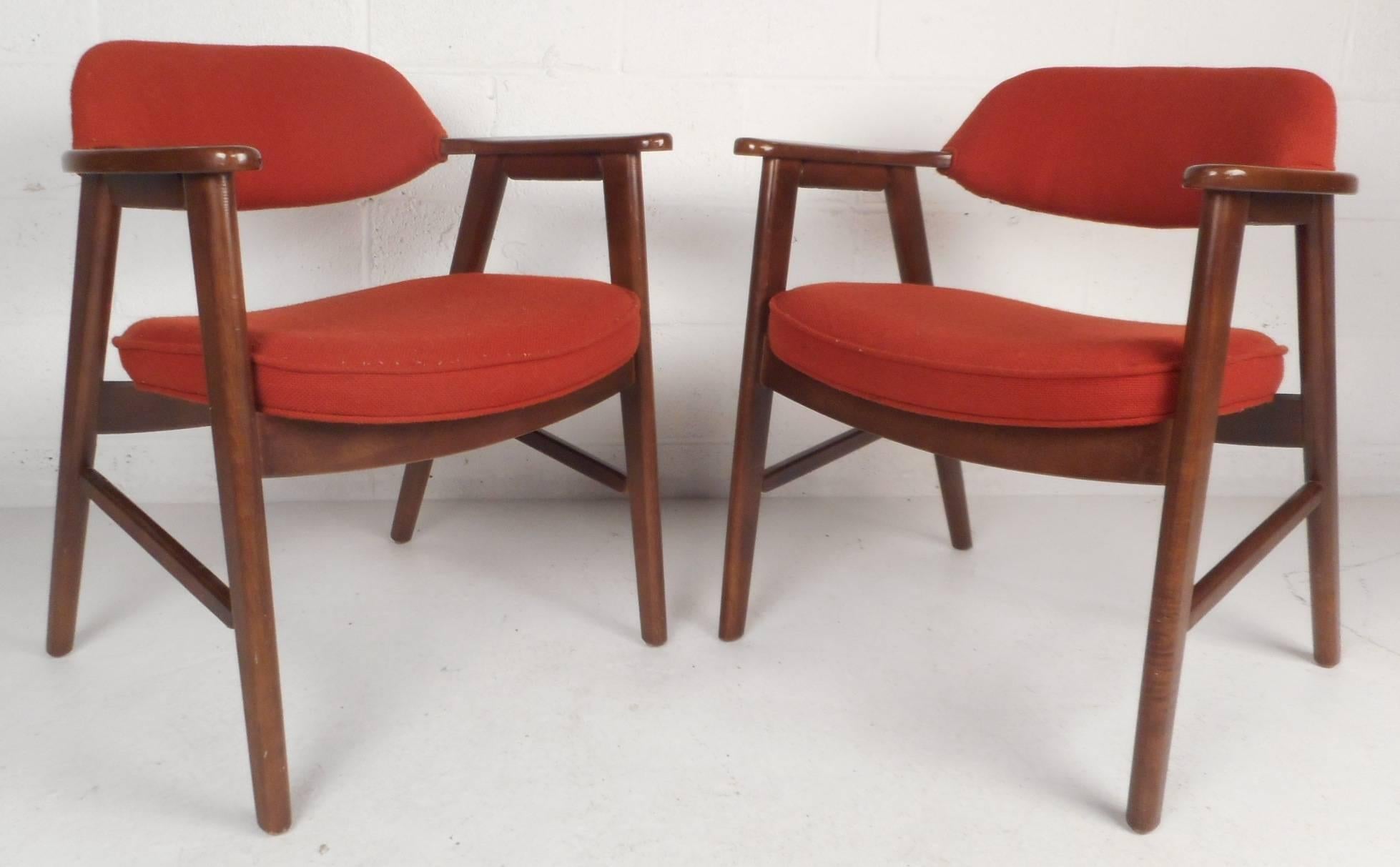 This beautiful pair of vintage modern side chairs feature a solid dark mahogany frame and plush red upholstery. Unique design has stylish cut-out arm rests and angled back legs. This sleek and sturdy Mid-Century Modern pair of arm chairs make the