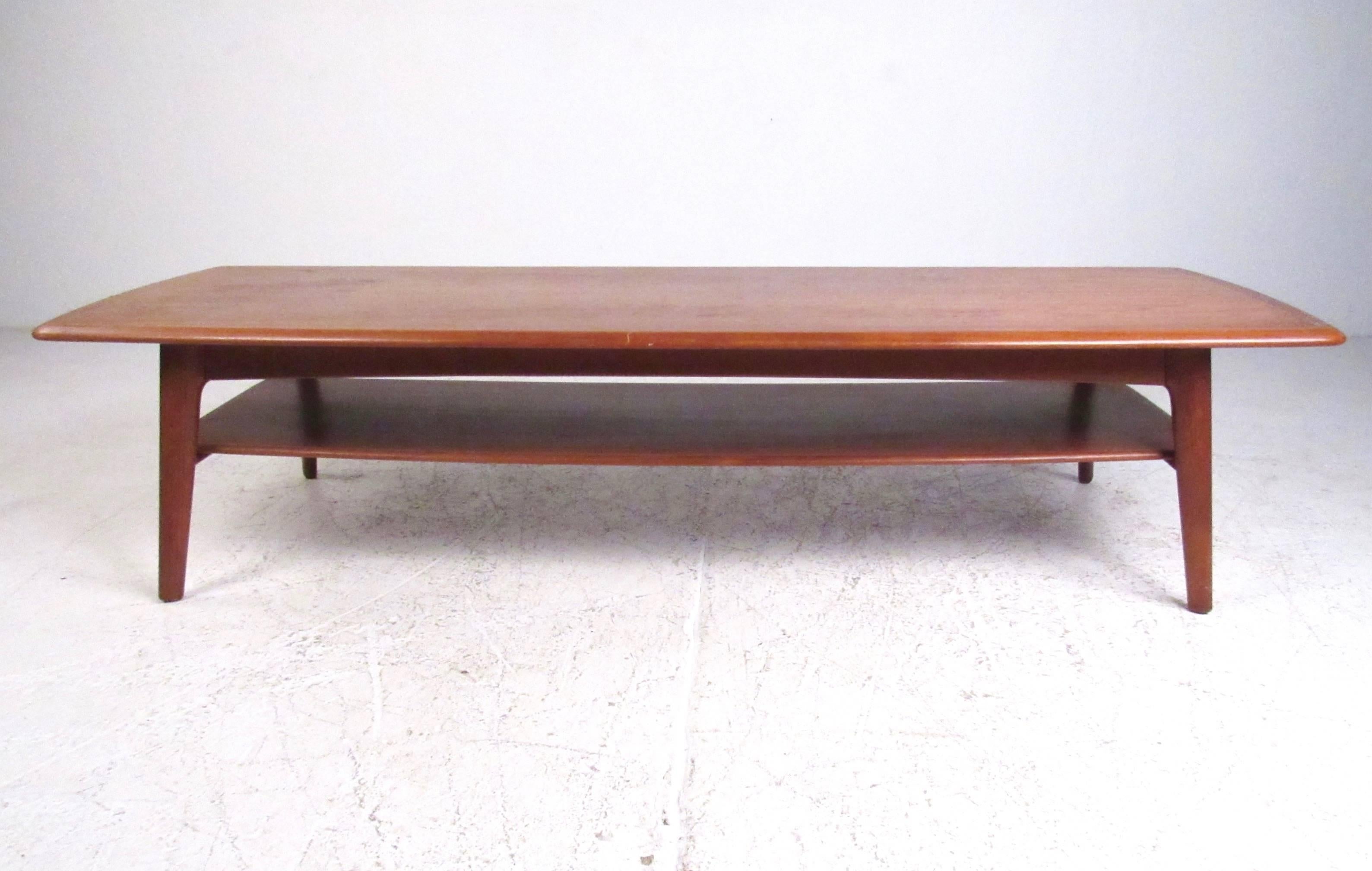 This unique vintage teak coffee table makes a substantial addition to any interior. At almost six feet long this impressive Danish Modern coffee table features tapered legs, shapely hardwood top, and a second tier storage shelf. Please confirm item