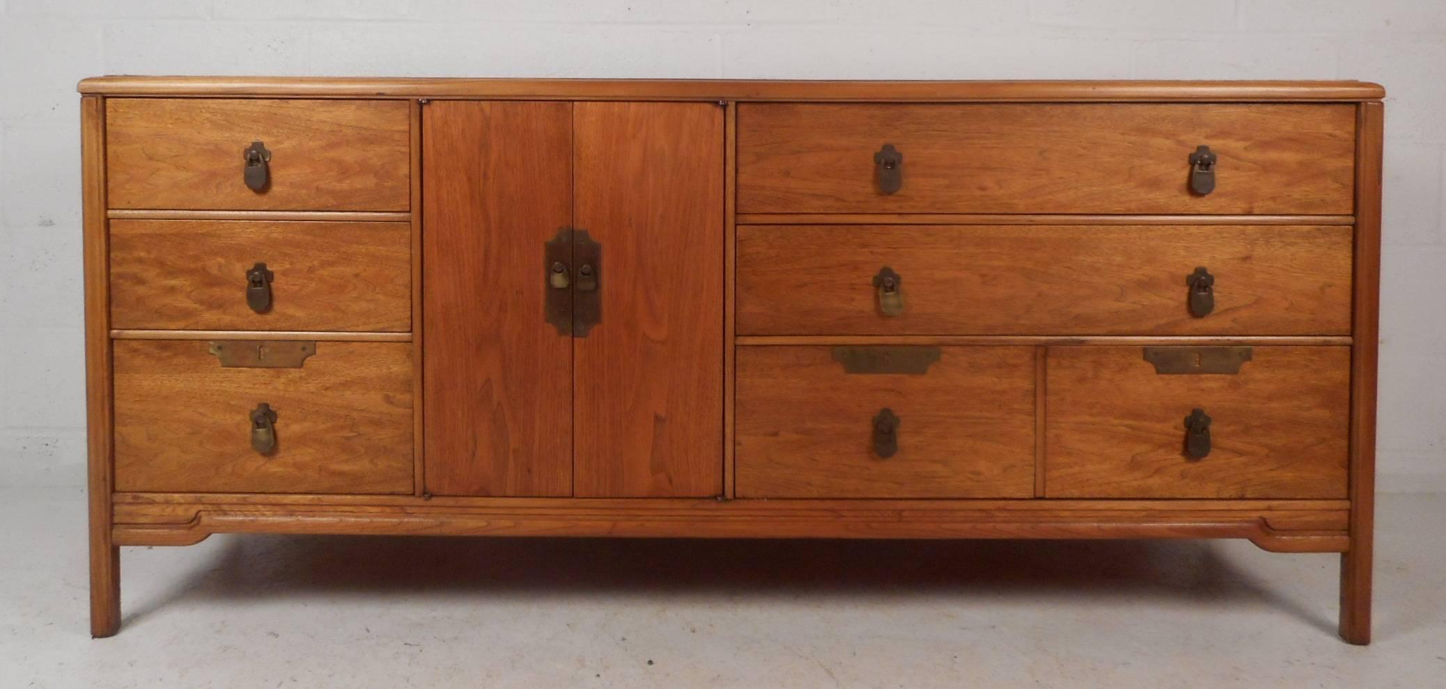 This stunning vintage modern dresser features nine hefty drawers with three hidden behind two cabinet doors. Sleek design with unique brass pulls on fixtures and stylish inlays on the top. This beautiful Mid-Century case piece has oak trim with