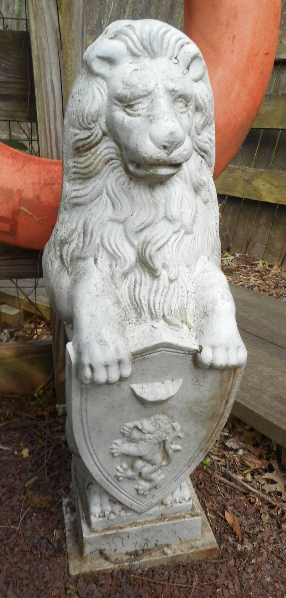 Gorgeous pair of lion statues made of cast iron holding a shield on a small pedestal base. Unique garden ornaments with intricate etched detail from the shield to the lions mane. This exquisite pair make the perfect addition to the entrance of any