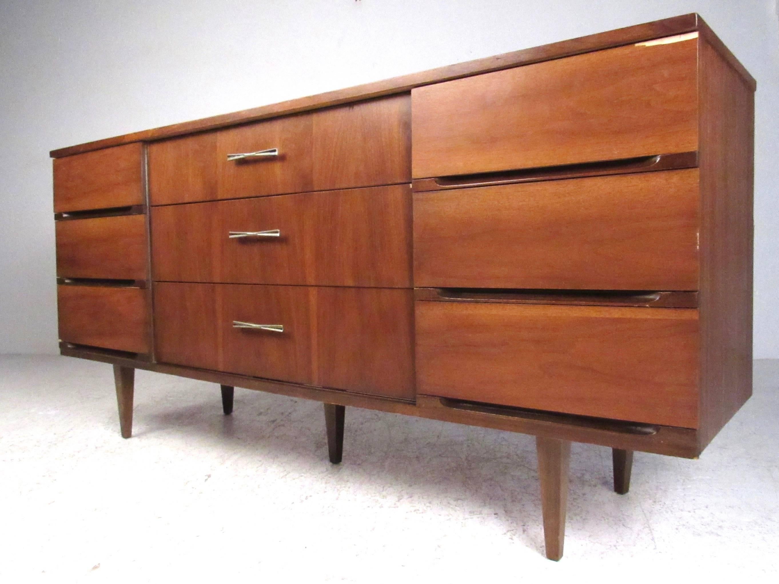 This Mid-Century Modern walnut dresser features nine spacious drawers for bedroom storage, tapered legs and unique drawer pulls. The clean modern lines and mixed walnut finish adds to the vintage appeal of the piece. Please confirm item location (NY