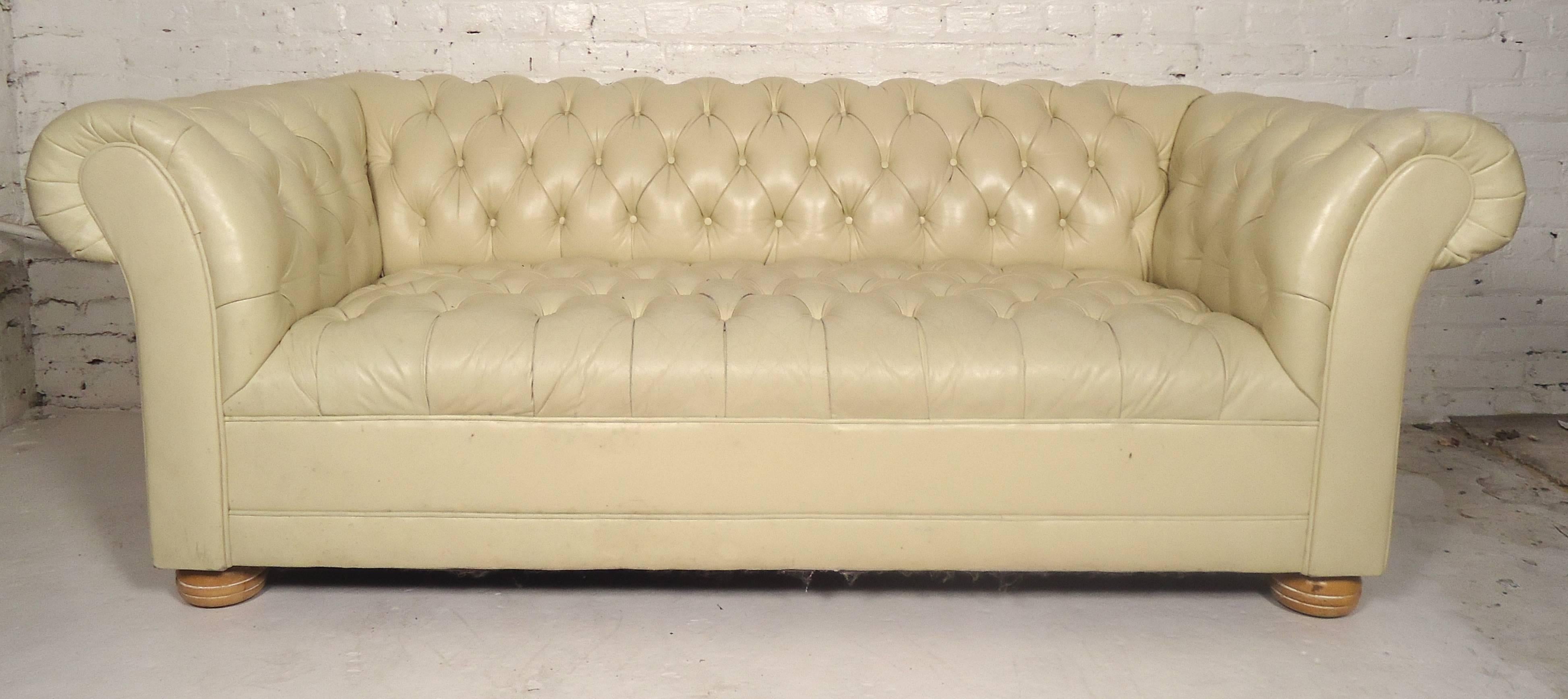Vintage off-white tufted sofa in soft leather. Classic Chesterfield style with large rolling arms and wooded feet.

(Please confirm item location - NY or NJ - with dealer).
  