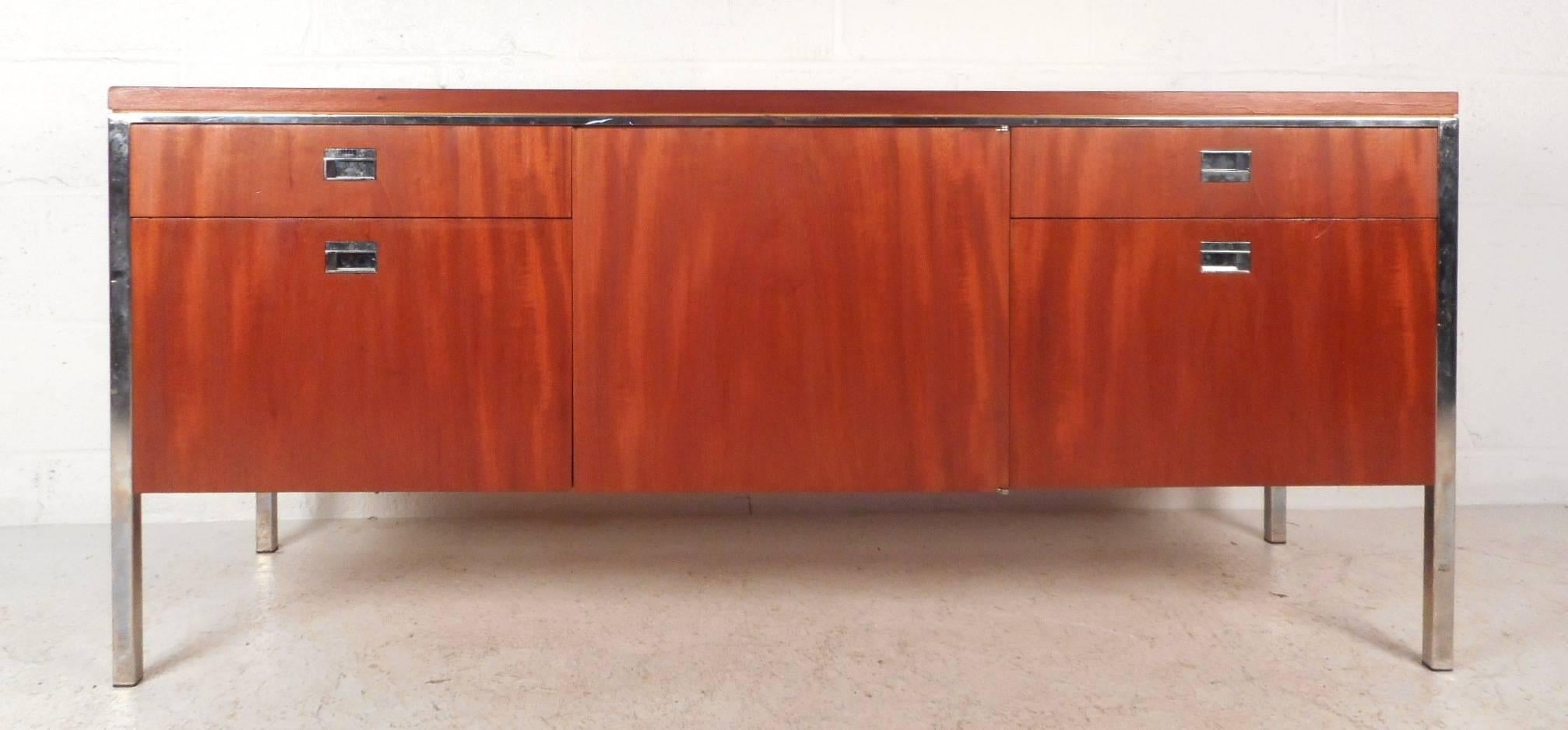 This beautiful vintage modern sideboard features four drawers for storage and a large compartment in the middle hidden by a cabinet door. Sleek design with unique chrome pulls and a sturdy chrome frame. This stylish Mid-Century case piece has