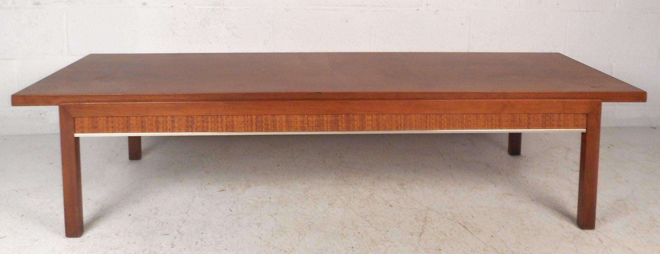 This stunning vintage modern coffee table features cane sides and a gorgeous walnut finish. Unique design with an oversized tabletop hangs over each side for added space. This straight line Mid-Century piece shows quality craftsmanship. This sleek
