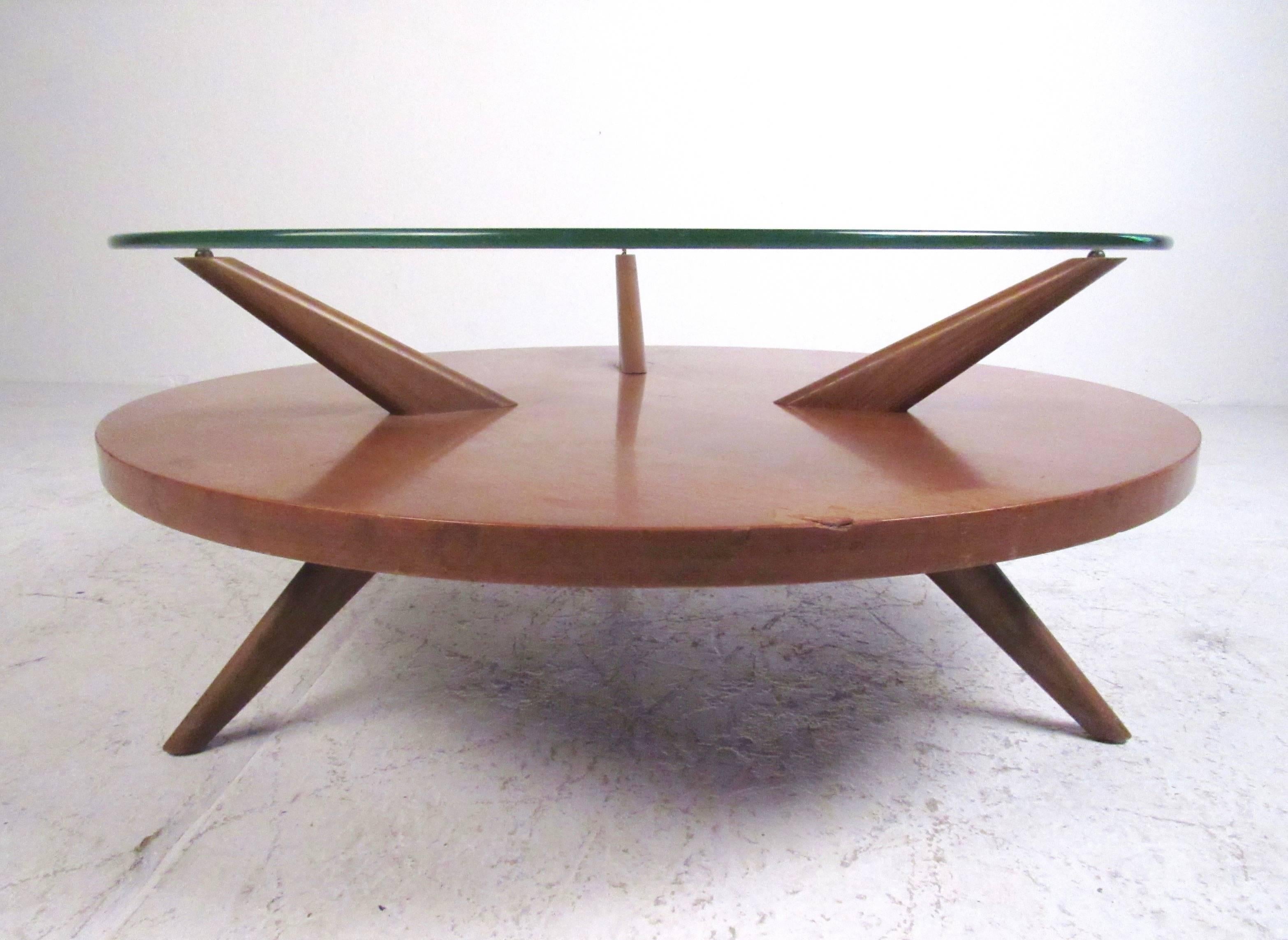 This vintage two-tier coffee table features sculpted legs, circular glass top, and vintage walnut finish. The Mid-Century Modern Heywood-Wakefield style of this table makes it an impressive addition to any seating area, please confirm item location