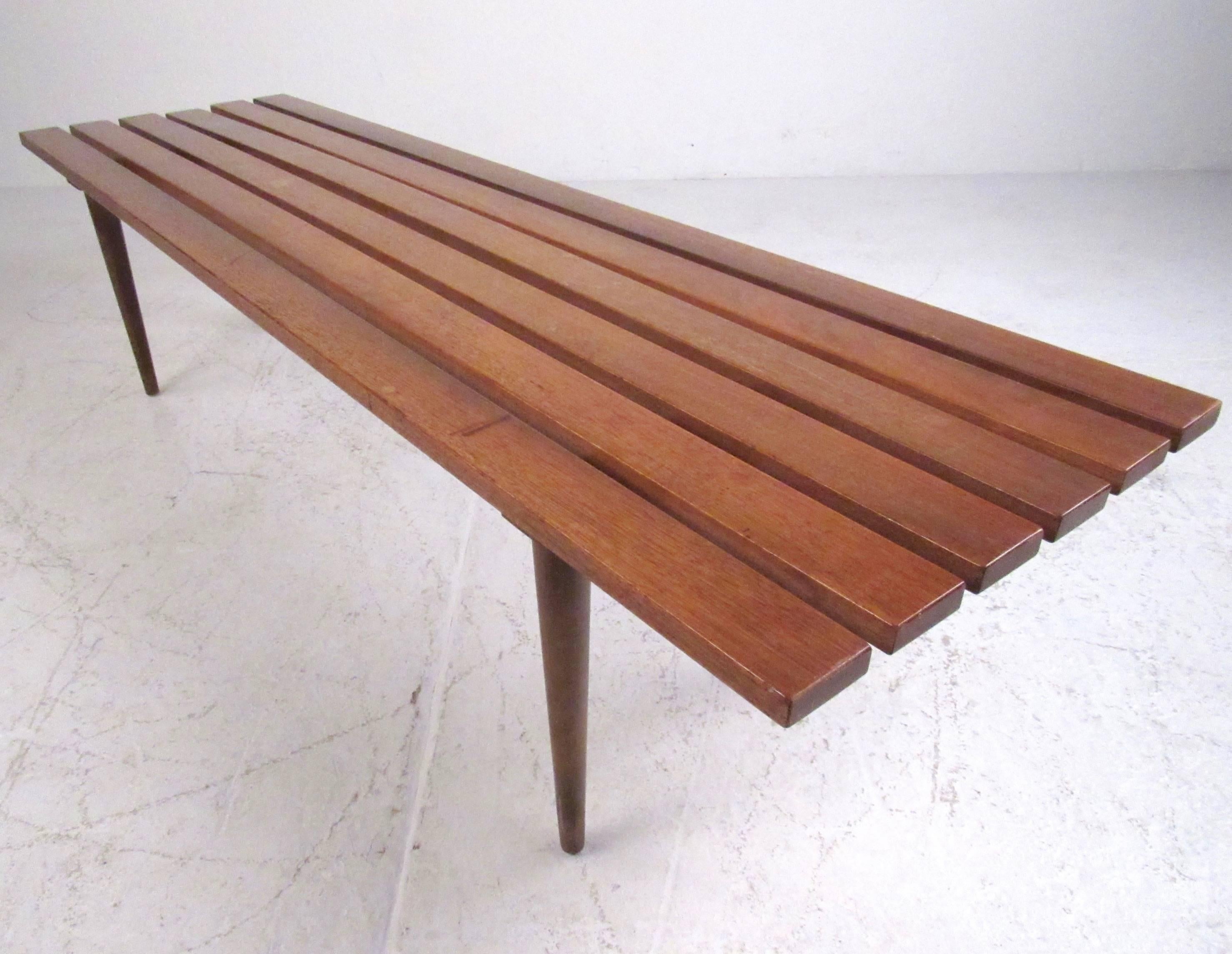 This hardwood slat bench features tapered legs and George Nelson style mid-century design. Standing at a height of 17.5 inches, this vintage modern slat bench makes the perfect piece for occasional seating or even as a tall coffee table. Please