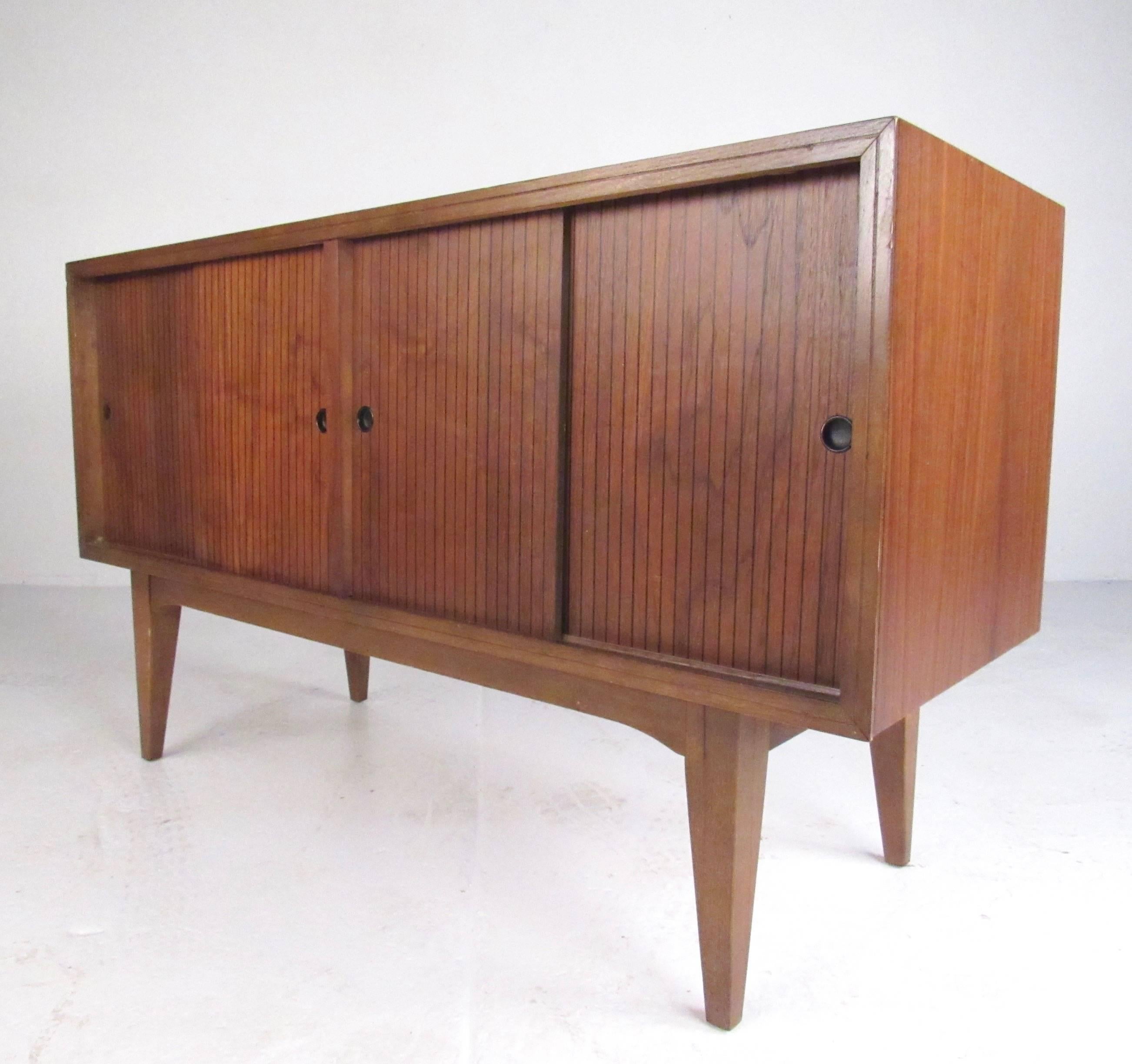 This uniquely sized vintage credenza features iconic Lane Furniture design with tapered legs, rich walnut finish, and slat style sliding doors. Petite size makes this Mid-Century Modern cabinet ideal for office storage or use as a media cabinet or